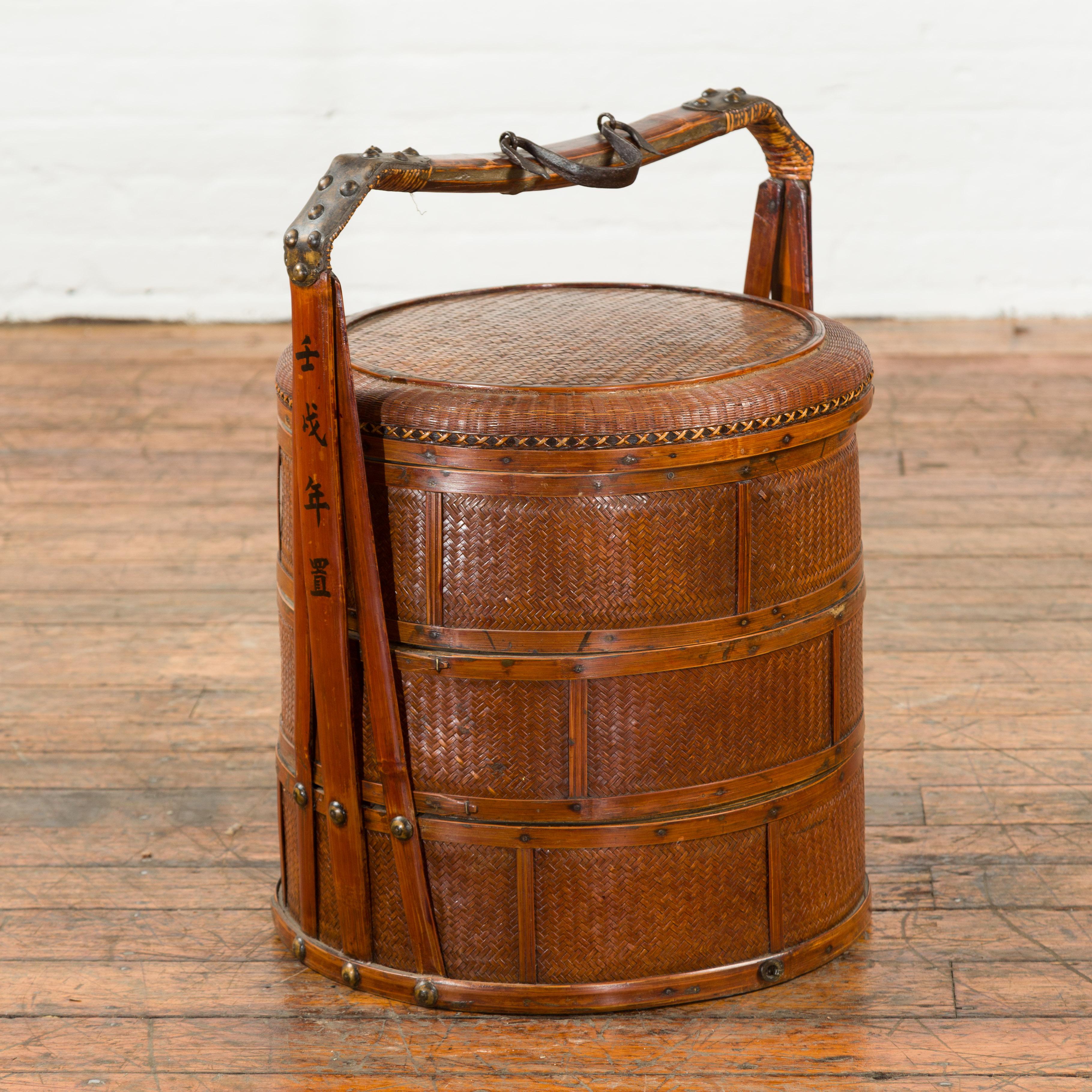 A Chinese antique rattan three-tiered nested food basket from the early 20th century, with calligraphy and iron accents. Created in China during the early years of the 20th century, this food basket features a circular lid, sitting above three