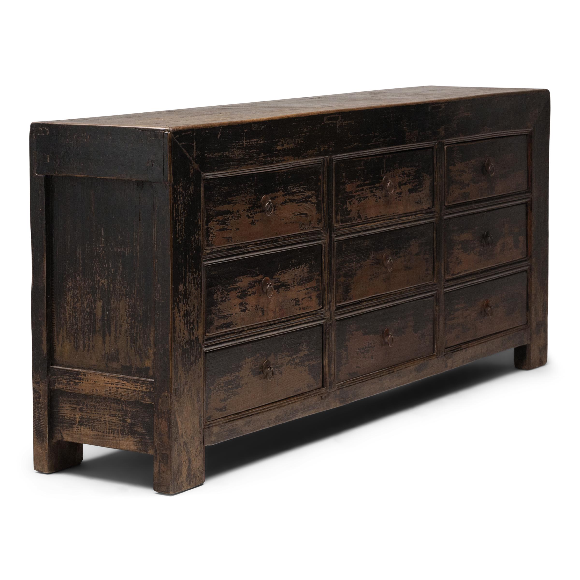 Questa cassapanca della fine del XIX secolo bilancia una silhouette snella con texture wabi-sabi. Originariamente configurato per aprirsi dall'alto, il frontale a pannelli del mobile è stato modificato in nove cassetti, ognuno dei quali è racchiuso