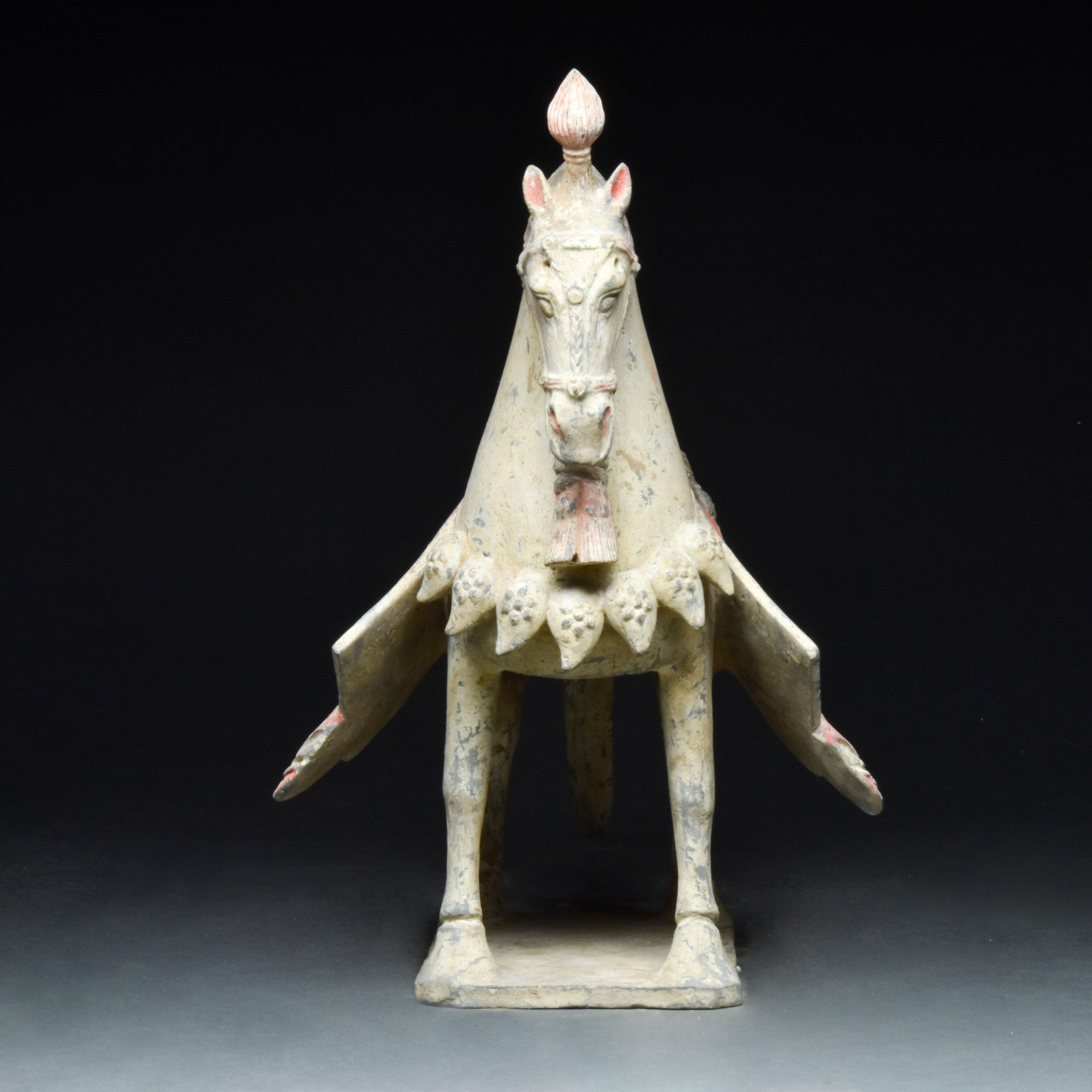 An elegant hollow-moulded terracotta horse. This horse is modelled in a standing pose with its neck elegantly arched and its ears pricked forward attentively. The mane is indicated with the use of a scalloped red design with white dotted details.