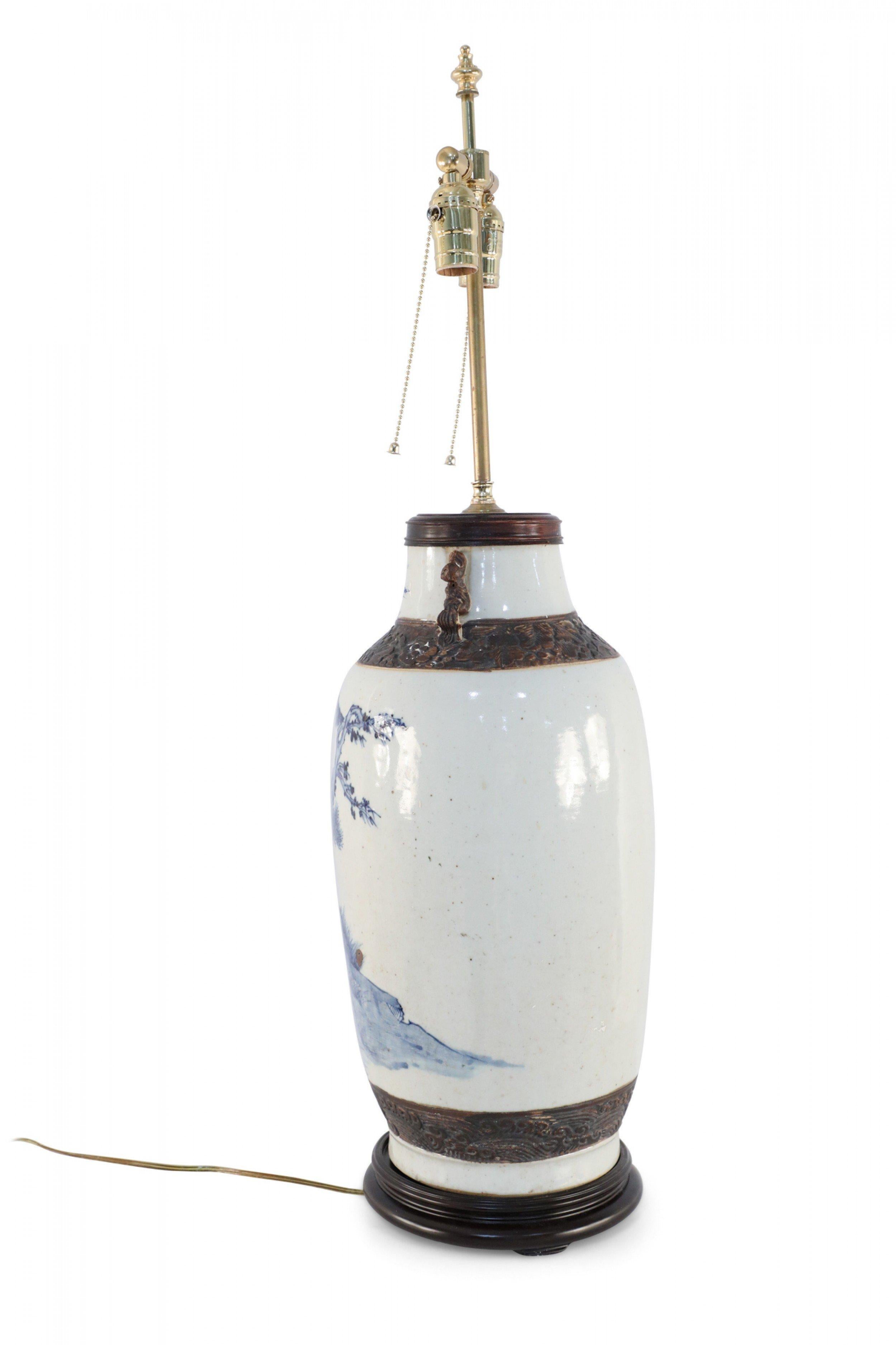 Antique Chinese (Late 19th Century) table lamp made from an off-white and blue stoneware vase with carved floral bands, two small decorative handles, and a scene depicting two women with umbrellas strolling in a pastoral setting on a wooden base.
 