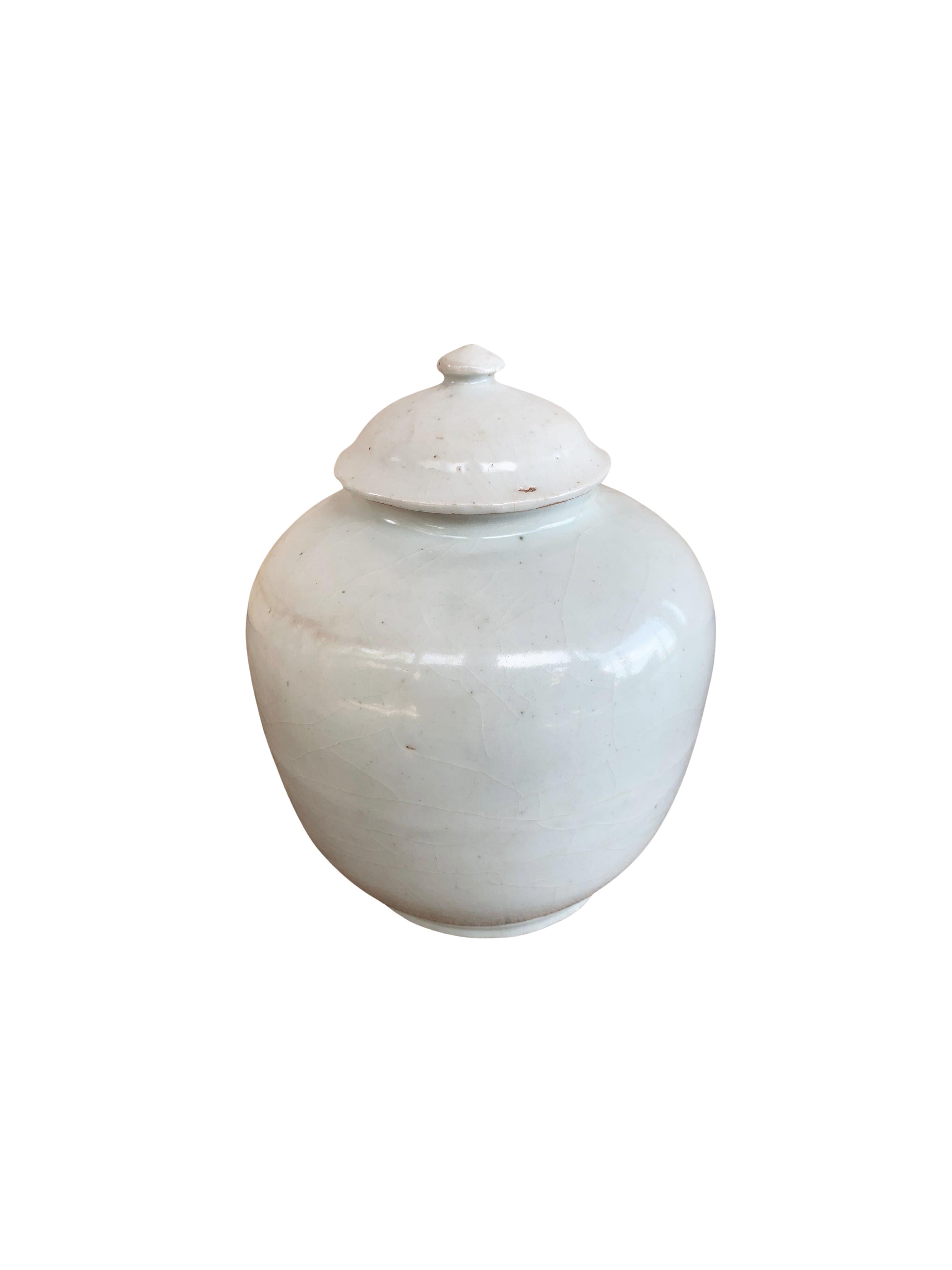 This ceramic ginger jar dates to the late 20th Century and orginates from China's Jiangxi province. It features an off-white and crackled glaze with a slight and very faint turquoise/blue tint. This Jar features a streamlined form with high