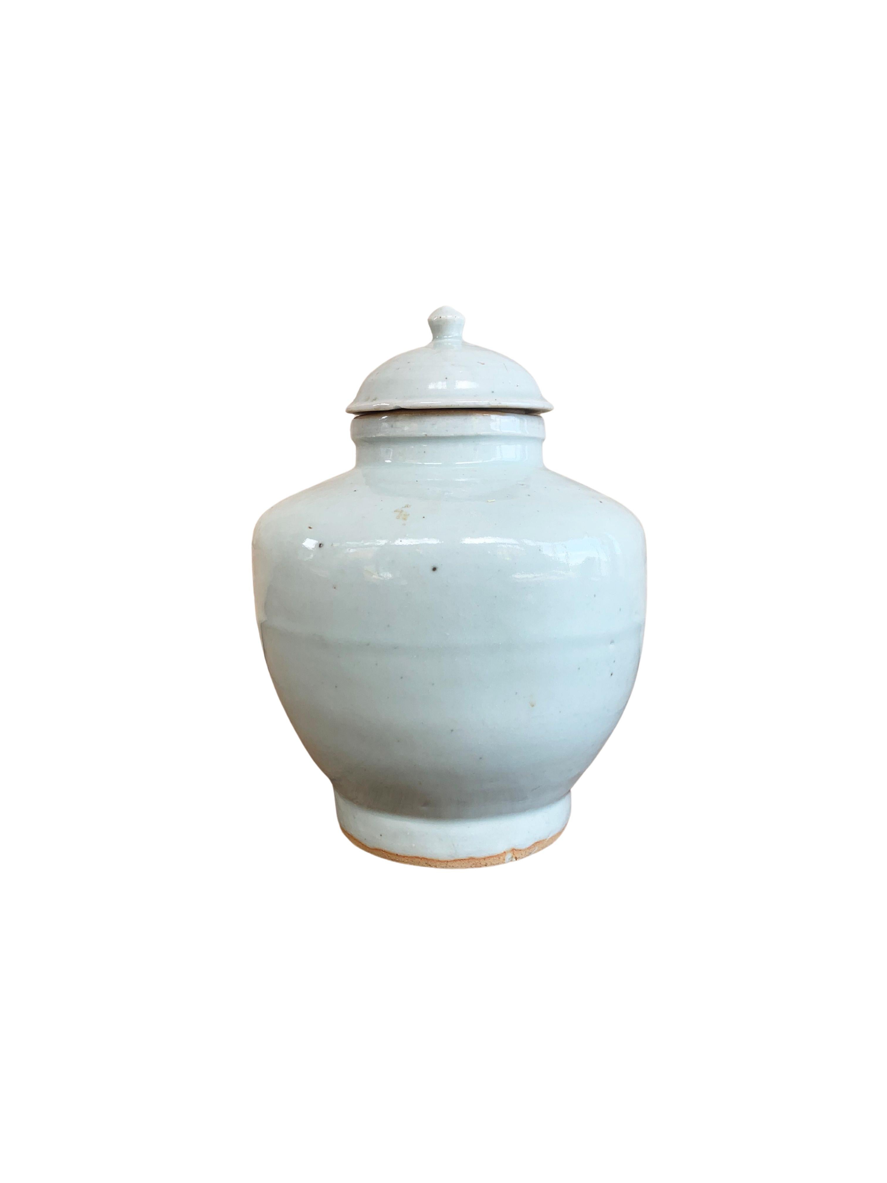 This ceramic ginger jar dates to the late 20th century and orginates from China's Jiangxi province. It features an off-white and crackled glaze with a slight and very faint turquoise/blue tint. This Jar features a streamlined form with high