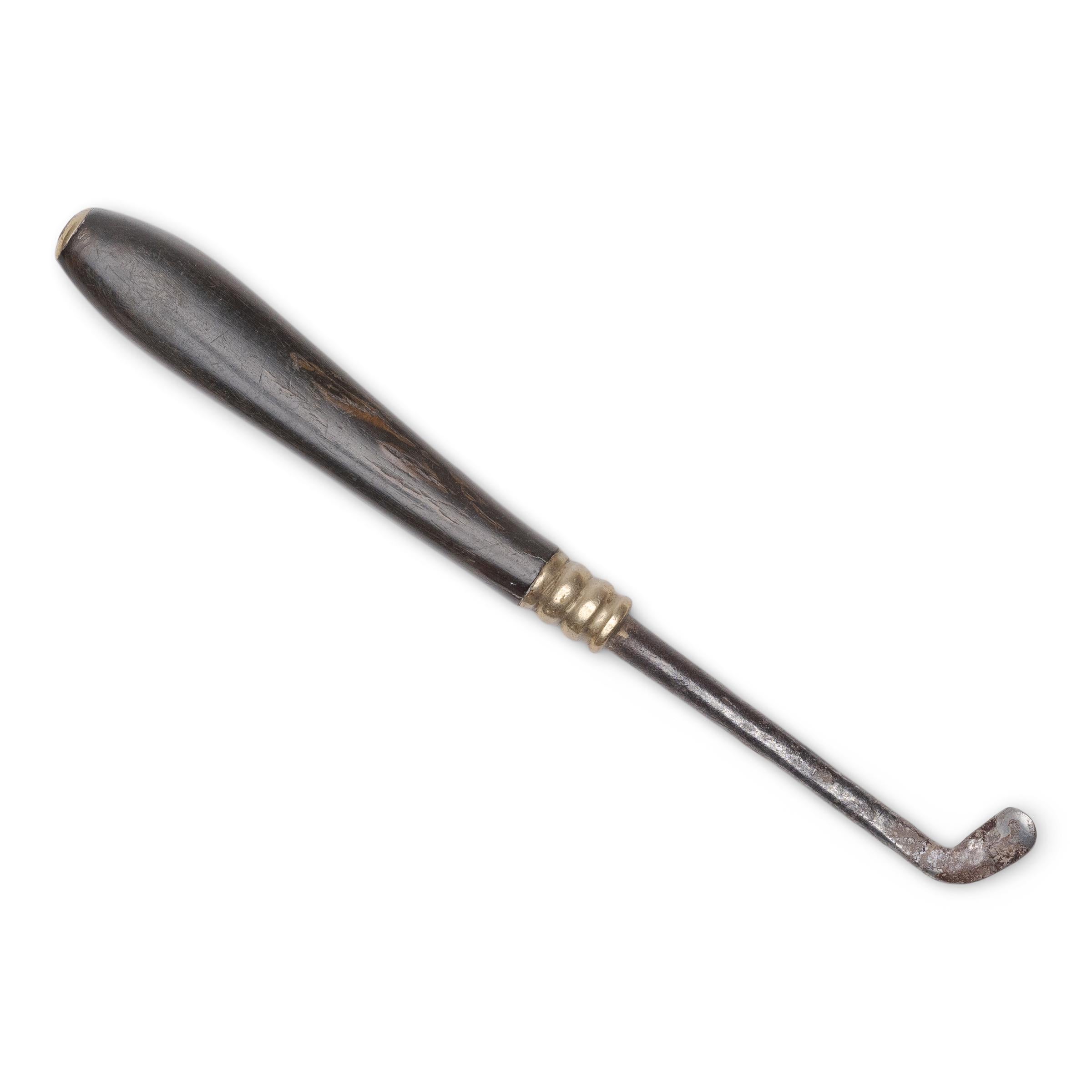 Cet outil portatif est un grattoir à opium du XIXe siècle, équipé d'une lame incurvée en forme de cuillère conçue pour retirer les débris des parois internes du fourneau d'une pipe. L'extrémité métallique est fixée à une élégante poignée effilée en