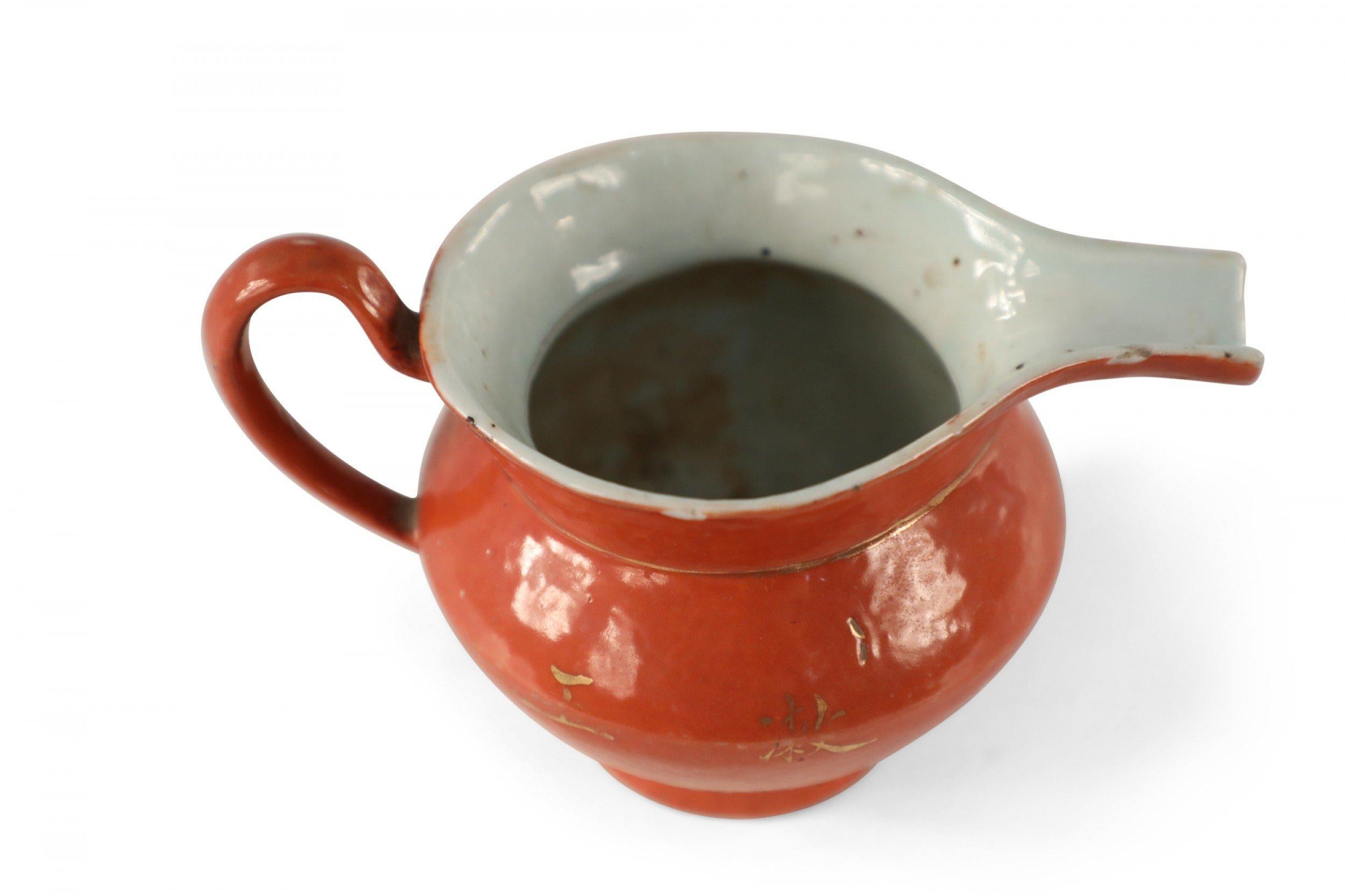 Chinese small orange porcelain pitcher decorated with gold botanicals and characters with a white interior.

Several small chips, wear to finish.