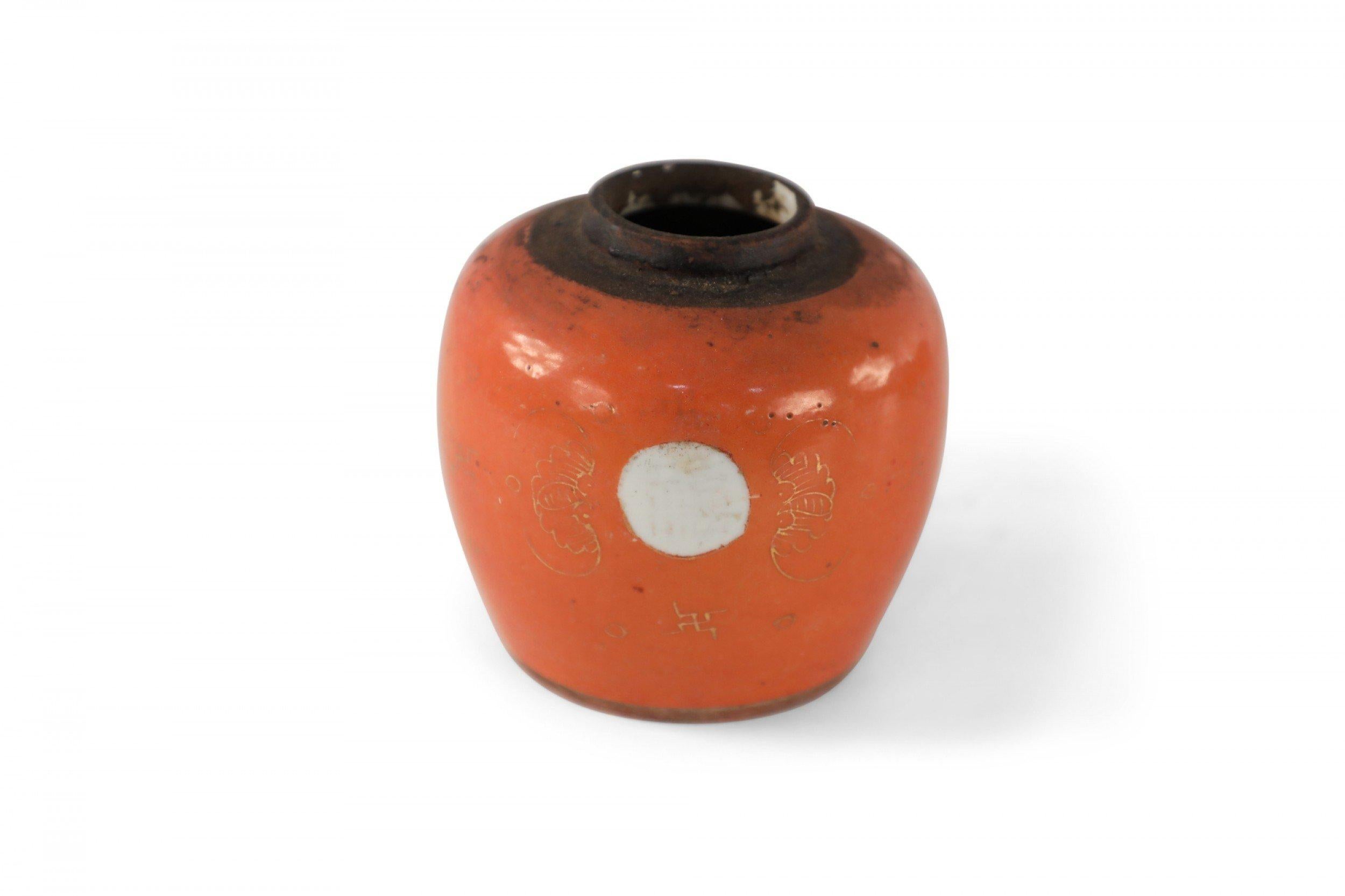 Chinese small, round orange porcelain vase with gold detailing surrounding white circular shapes and a brown band around the mouth opening.
 