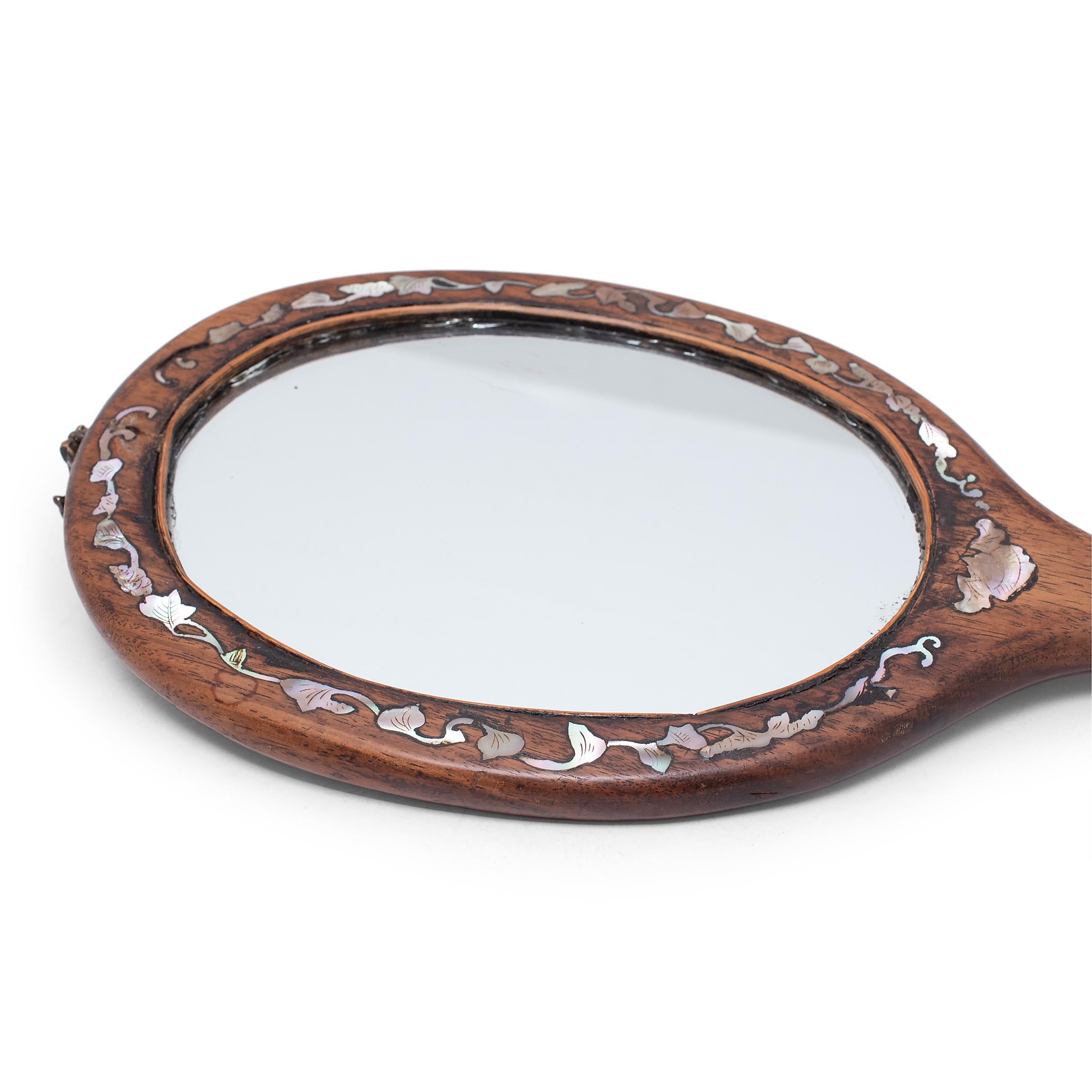 This large, early 20th-century hand mirror is set in a fine hardwood frame decorated with mother-of-pearl inlay of flowering vines. The handle is decorated with plum blossoms and a bat with outstretched wings, a symbol of joy and happiness. Each