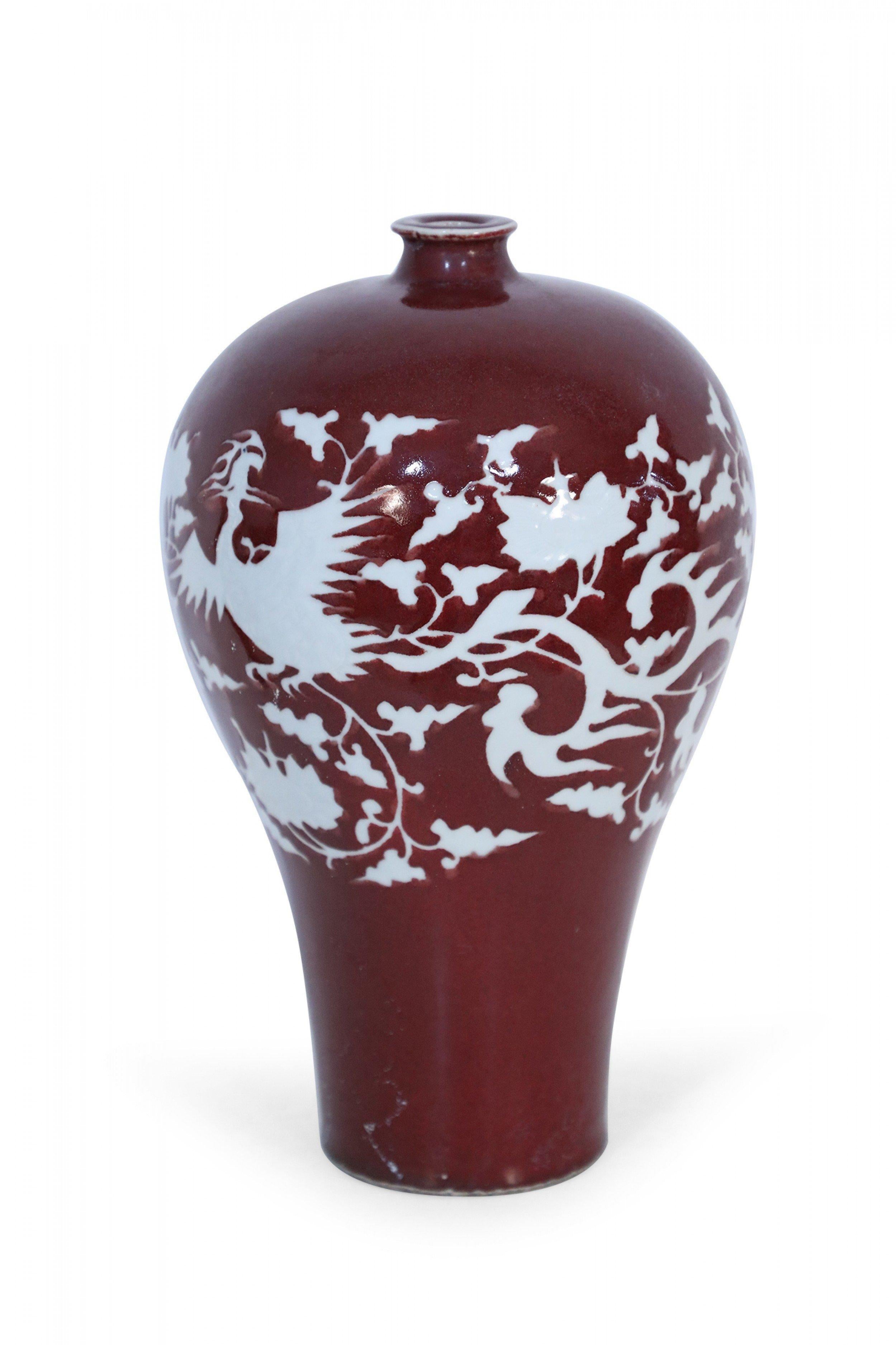 Vaso Meiping in porcellana cinese di colore rosso sangue decorato con un motivo naturale bianco che riprende le sagome di uccelli, viti e foglie.