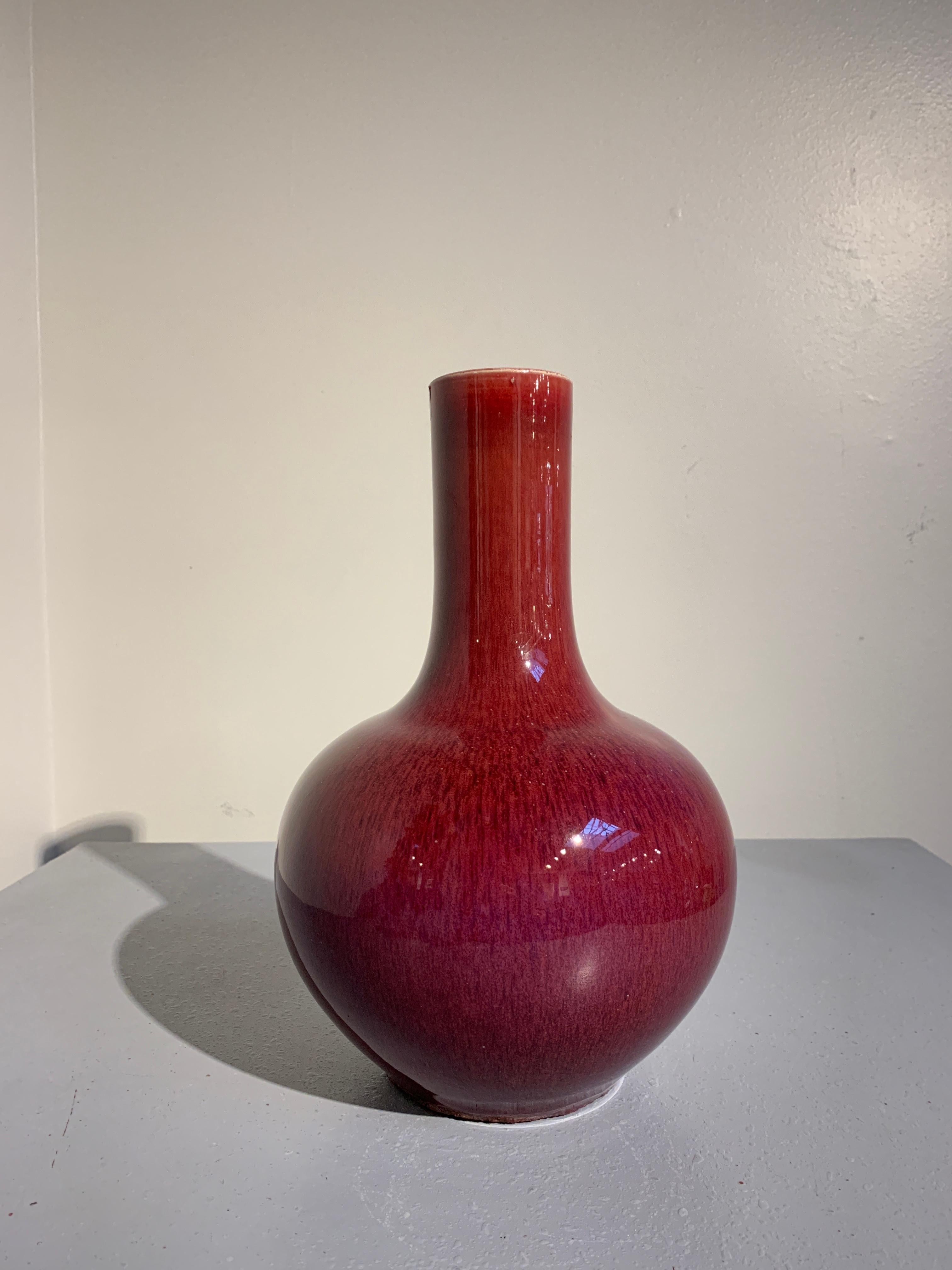 A stunning Chinese late Qing dynasty langyao monochrome red glazed tianquiping bottle vase, 19th century. 

Of bottle form, the vase with a globular body and tall, wide neck, all sitting upon a short recessed foot and covered in a fascinating