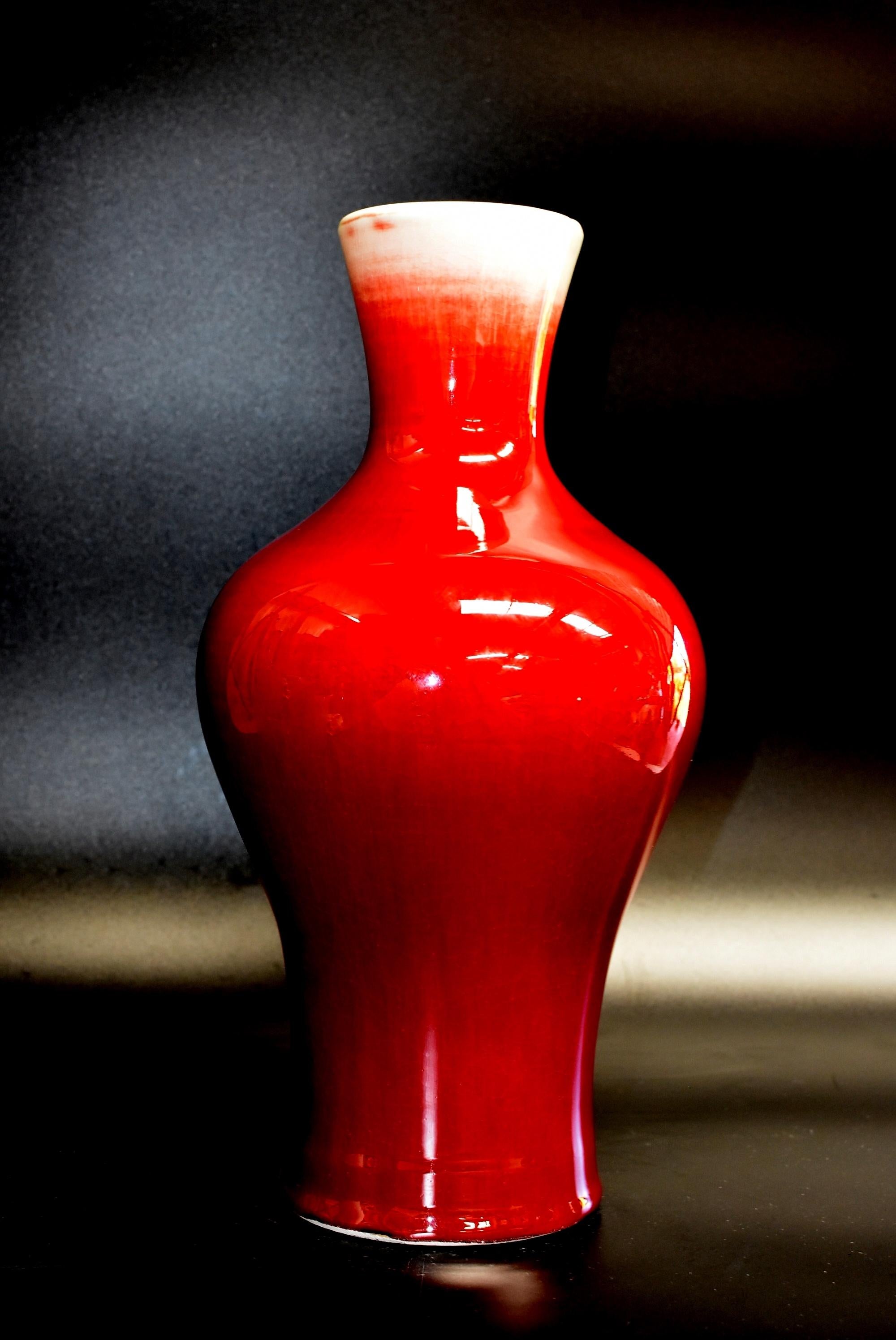 A beautiful Sang-De-Boef vase. The baluster body rising from a spreading foot to a waisted neck, the exterior covered in a rich red glaze thinning to a mushroom tone near the rim, interior glazed white, inscribed to the base with a Jin De Zhen kiln