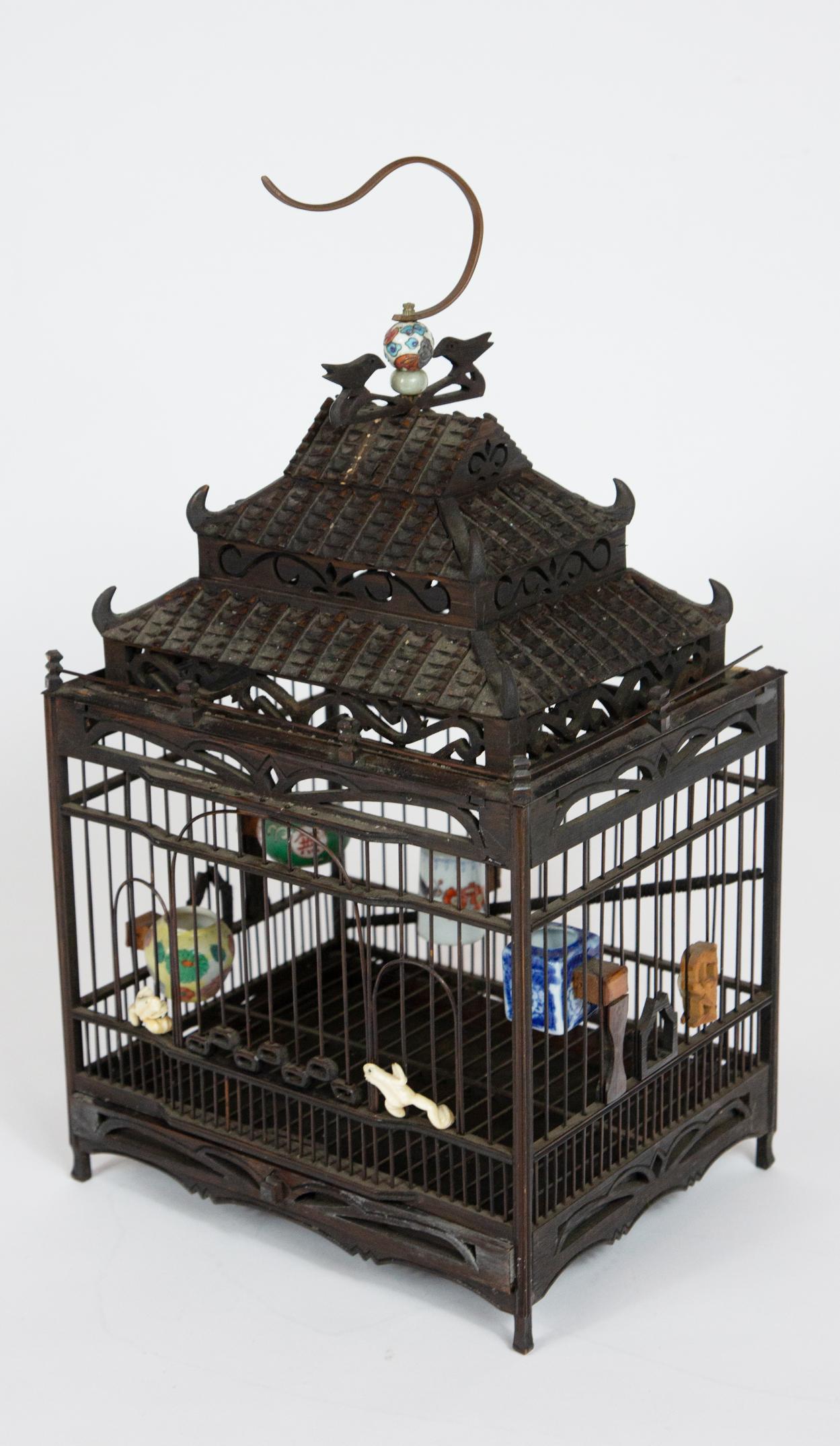 Carved open work wooden birdcage with tiered pagoda roof and miniature porcelain vessels.

Measures: 9