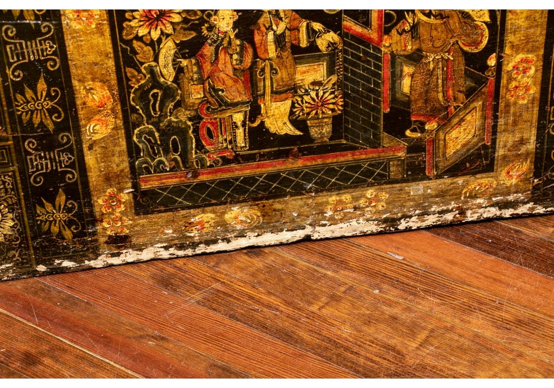 Eine Truhe aus ebonisiertem Holz mit gemaltem Dekor auf der Vorderseite. Die mittlere Tafel zeigt Damen in feinen Gewändern in einem von Blumen umrahmten Interieur. Eine Besucherin mit Kopfbedeckung und Fächer steht rechts an der Tür. Vergoldete