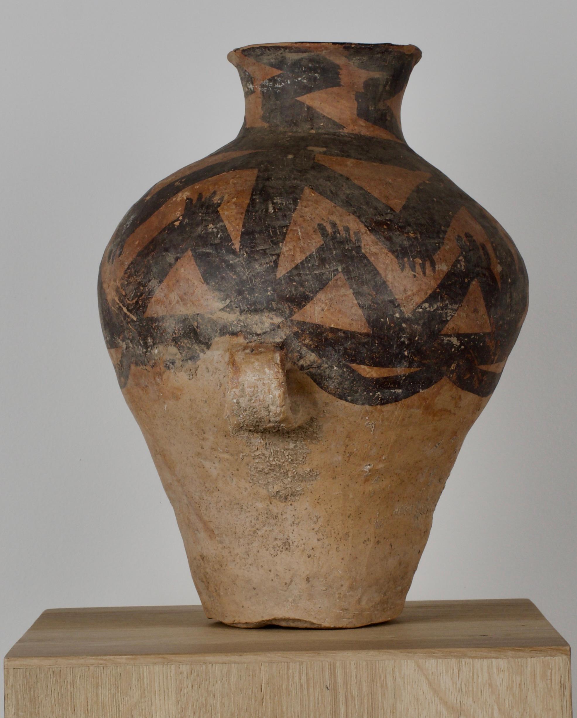 Bellissimo vaso dal corpo piriforme, collo a vita, bordo estroflesso e sezione rettangolare integrale con manici ad anello, bande circonferenziali dipinte con motivi geometrici di cerchi tratteggiati, chevron e mani. Questo manufatto storicamente
