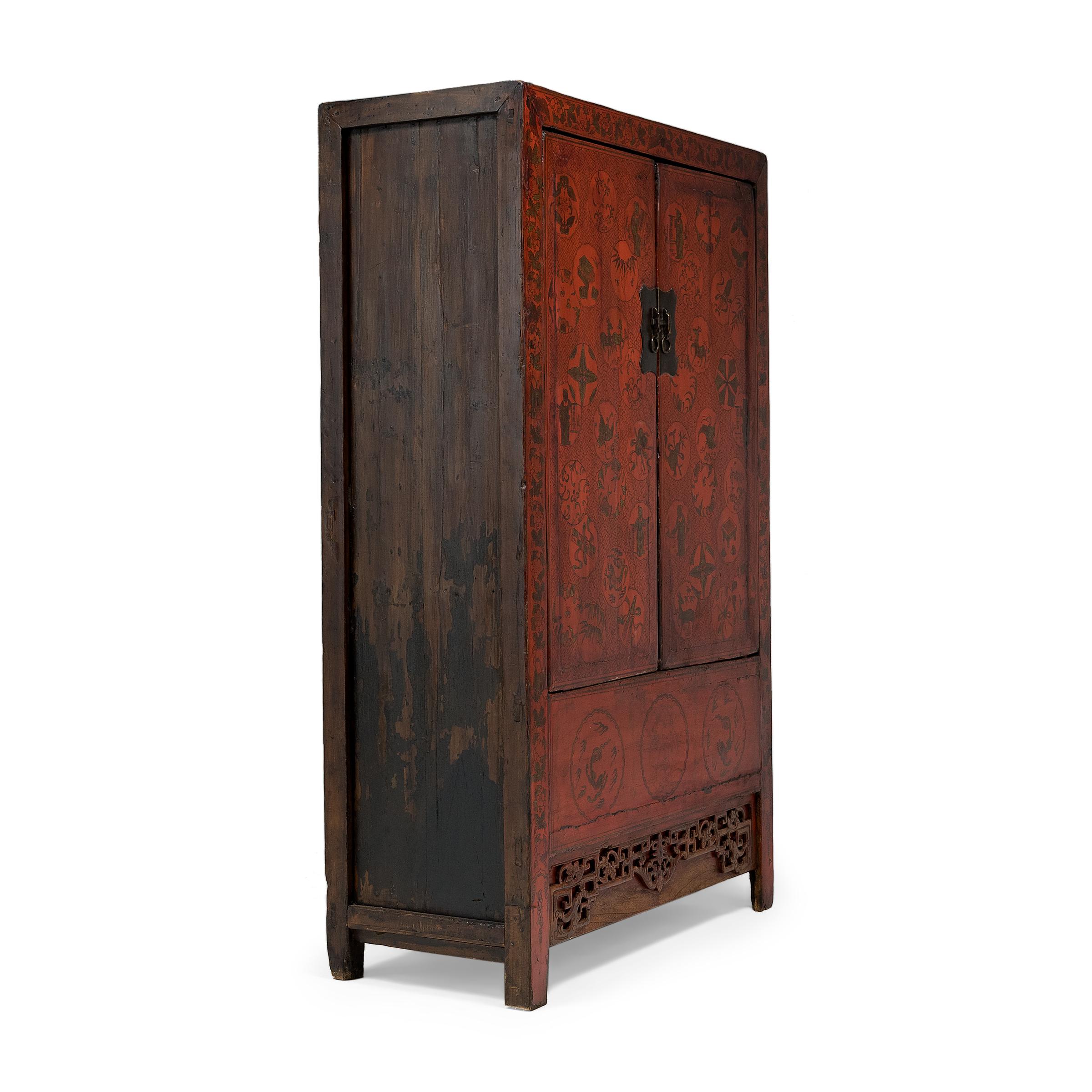 This early 20th century red lacquer cabinet is lavishly decorated with gilt accents and intricate, hand-painted line work. The tall cabinet has a clean-lined form, designed with straight sides, square corners and an ornately carved apron. The front