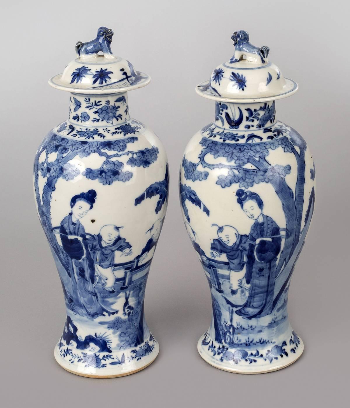 Pair of Chinese porcelain baluster-shaped lidded vases decorated with an elegant lady and two children playing under a banana tree. The neck and shoulder decorated with flowers and foliage. The lids have foo dog finials. Four character mark on