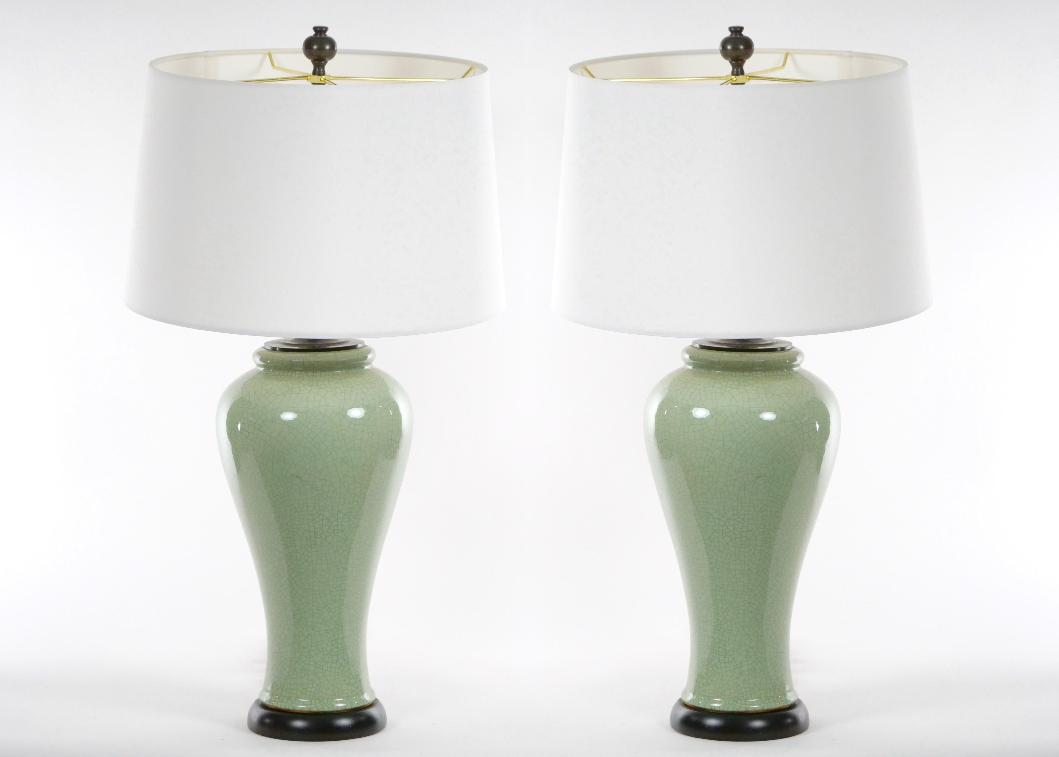 Mid-20th century pair of Chinese celadon green crackle porcelain baluster form vase table lamp with painted round wooden base. Each lamp is in great working condition and features a dimmable switch cord. Each lamp comes with a round drum shade. Each