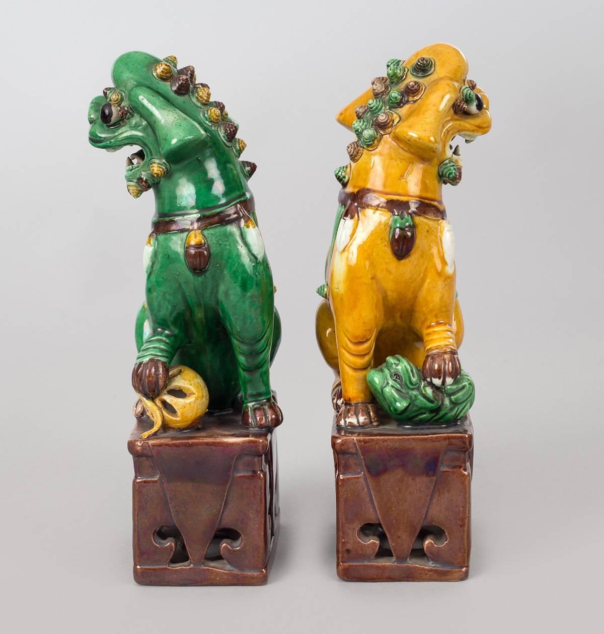Chinese pair of porcelain multi-colored foo dogs; the female is yellow and the male is green. They are both mounted on brown pierced bases.