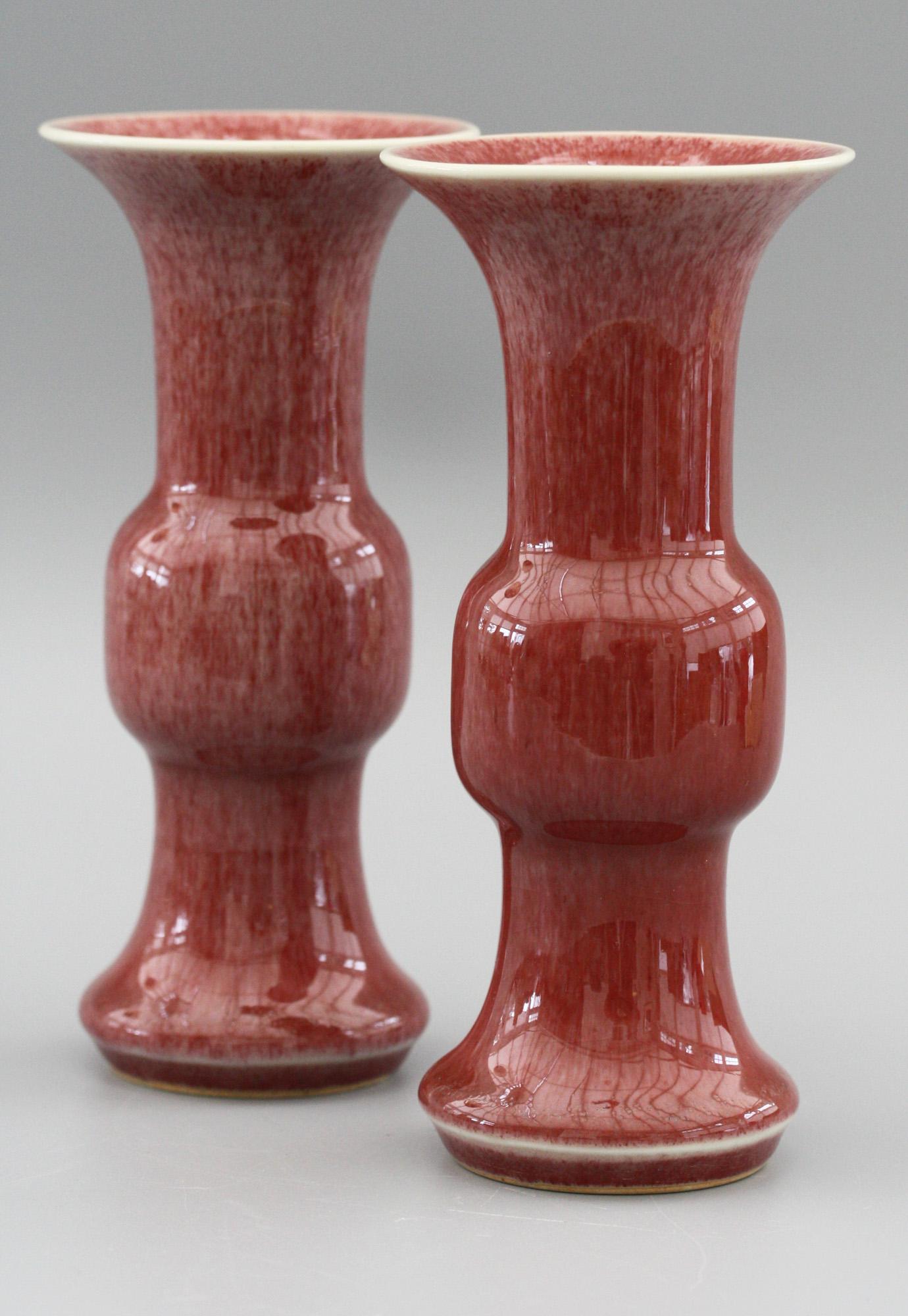 A fine and decorative pair Chinese Qianlong marked gu shaped porcelain vases decorated in red sang de boeuf glazes dating from the 20th century. The vases each have unglazed rounded feet with a skirted foot rim, a bulbous knop shaped body and