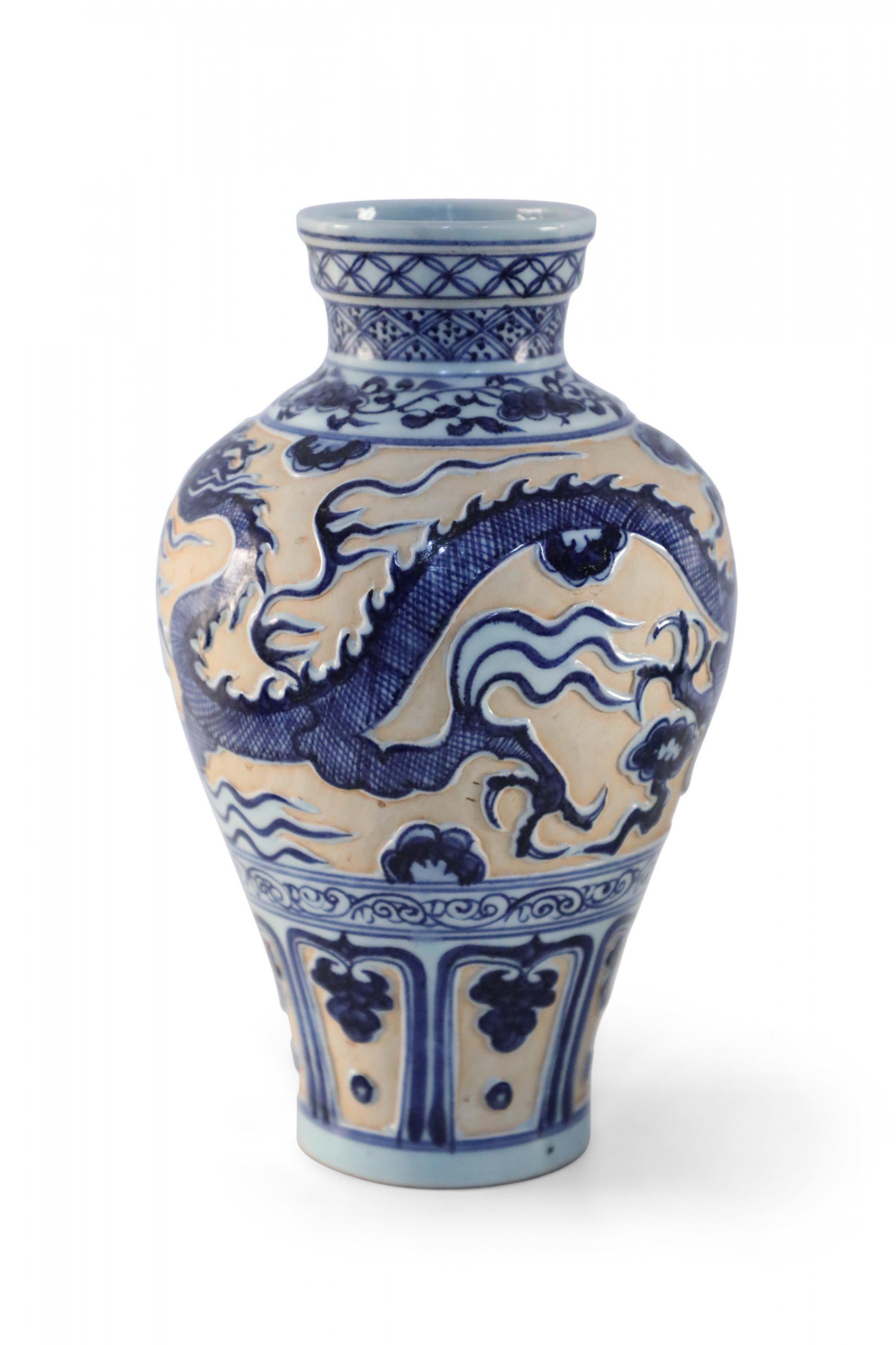 Chinese porcelain vase crafted in the style of the Yuan Dynasty depicting a raised and glazed blue and white dragon against a matte, peach colored ground, and decorated with geometric patterned bands around the opening.
    