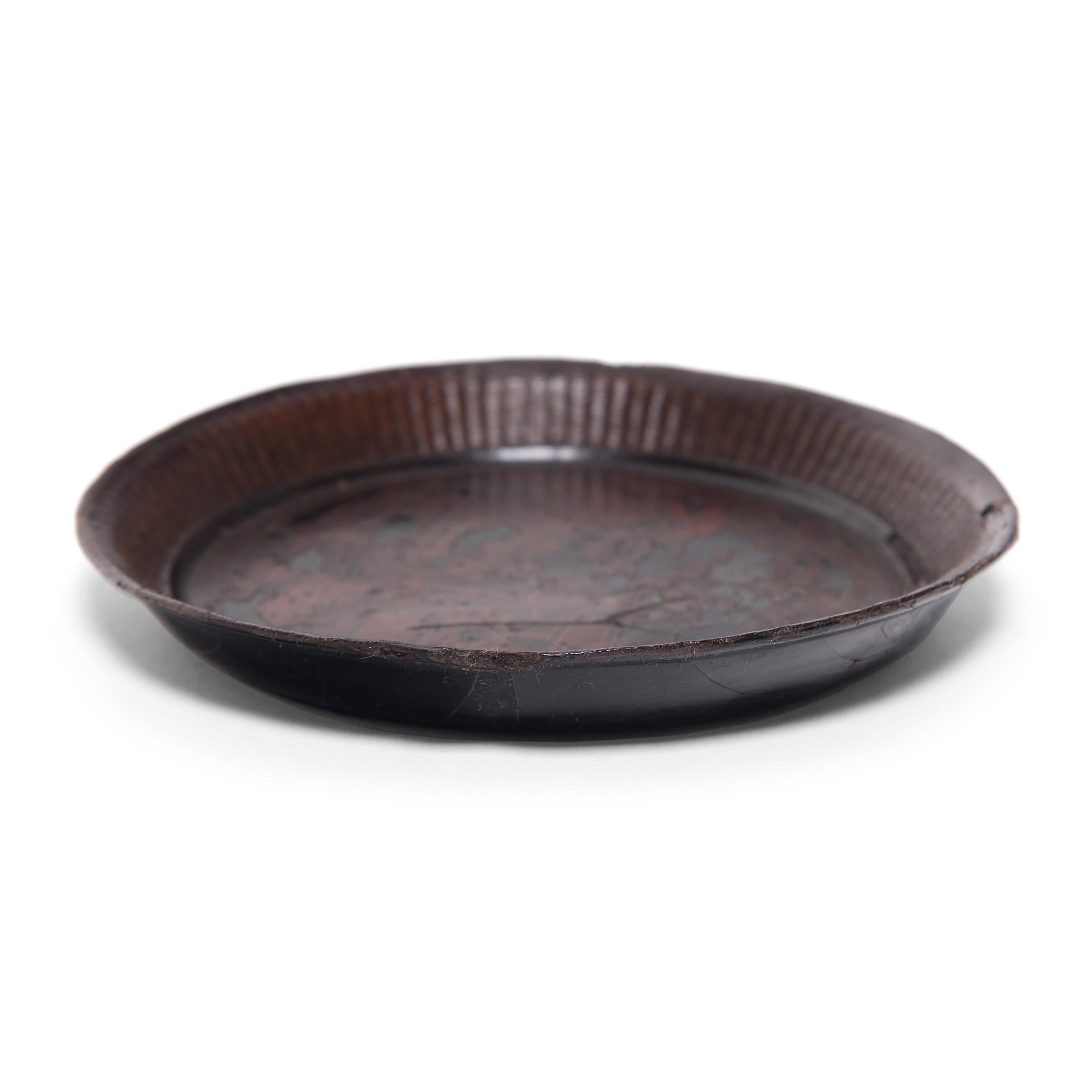 Dated to the mid-19th century, this small, round tray was likely once used as a shallow offering bowl atop a home altar. Comprised of finely woven bamboo sides and a thin wooden base, the plate is coated with dark black lacquer and decorated with a