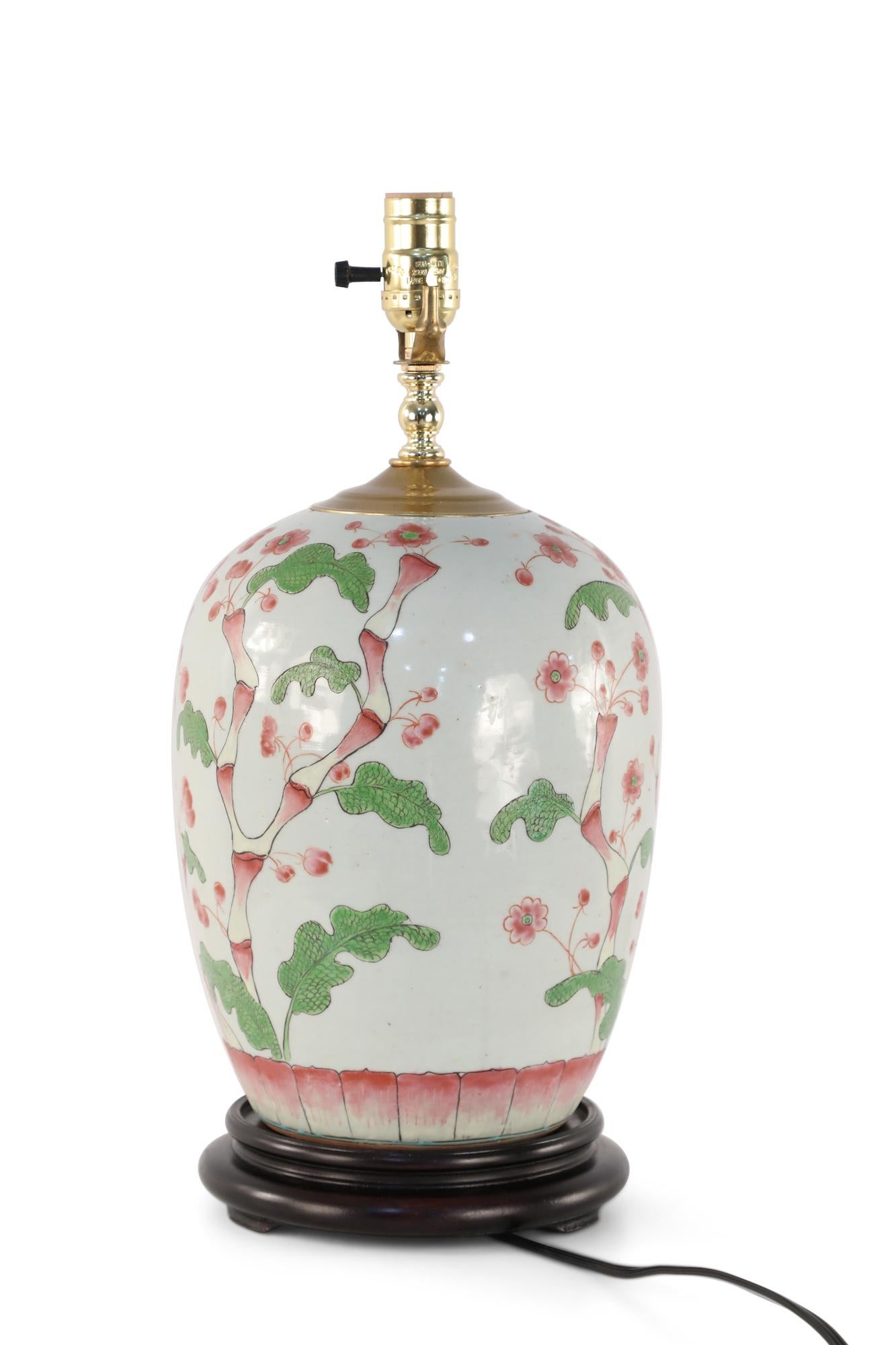 Chinese off-white porcelain table lamp made from a bulbous vase with a budding green and pink cherry blossom tree growing up its form, a wooden base, and brass hardware.
