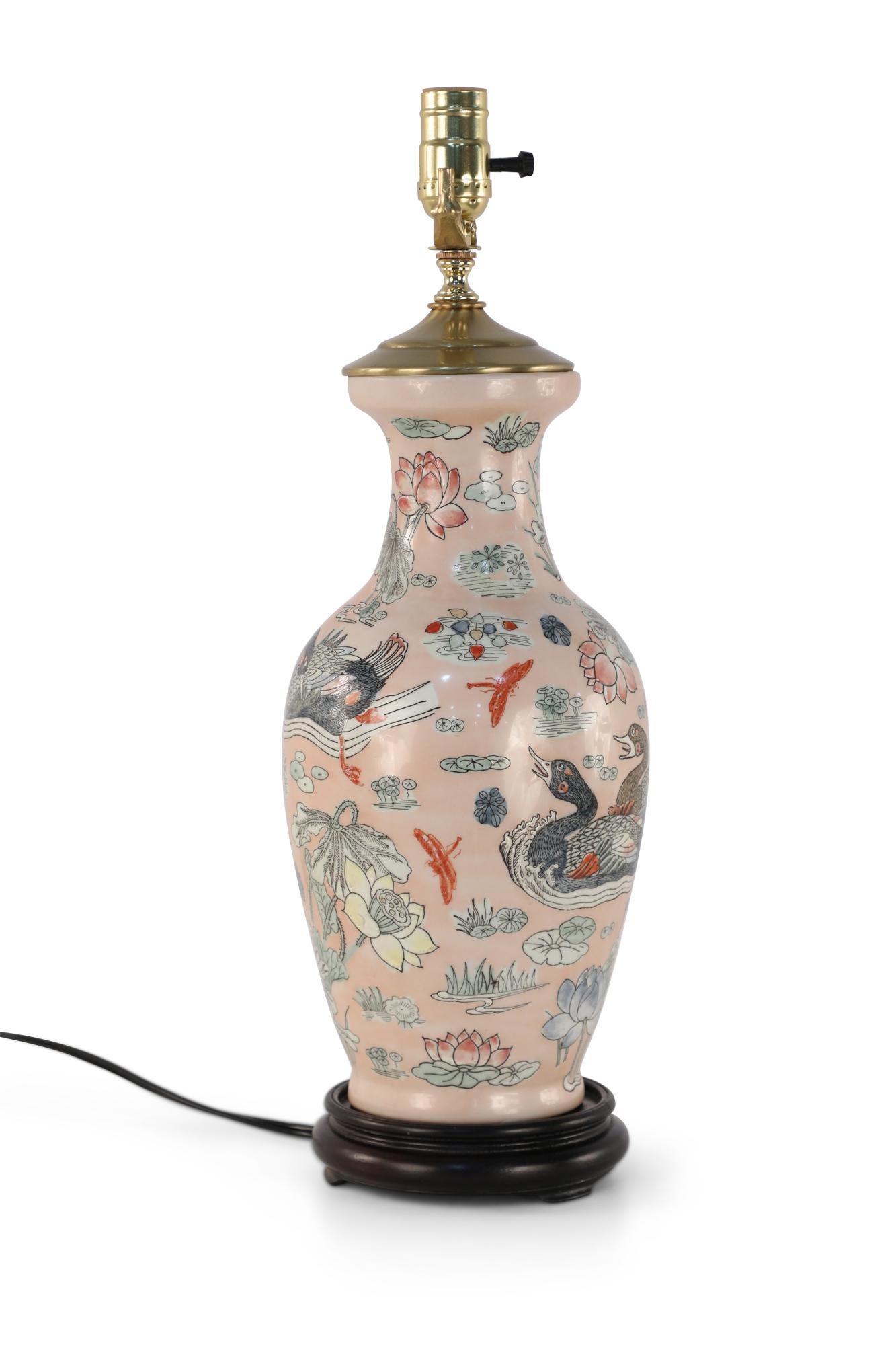 Chinese pink ceramic table lamp made from a baluster-shaped vase decorated with ducks in natural surroundings emphasized with linework and orange dragonflies, on a wooden base with brass hardware.