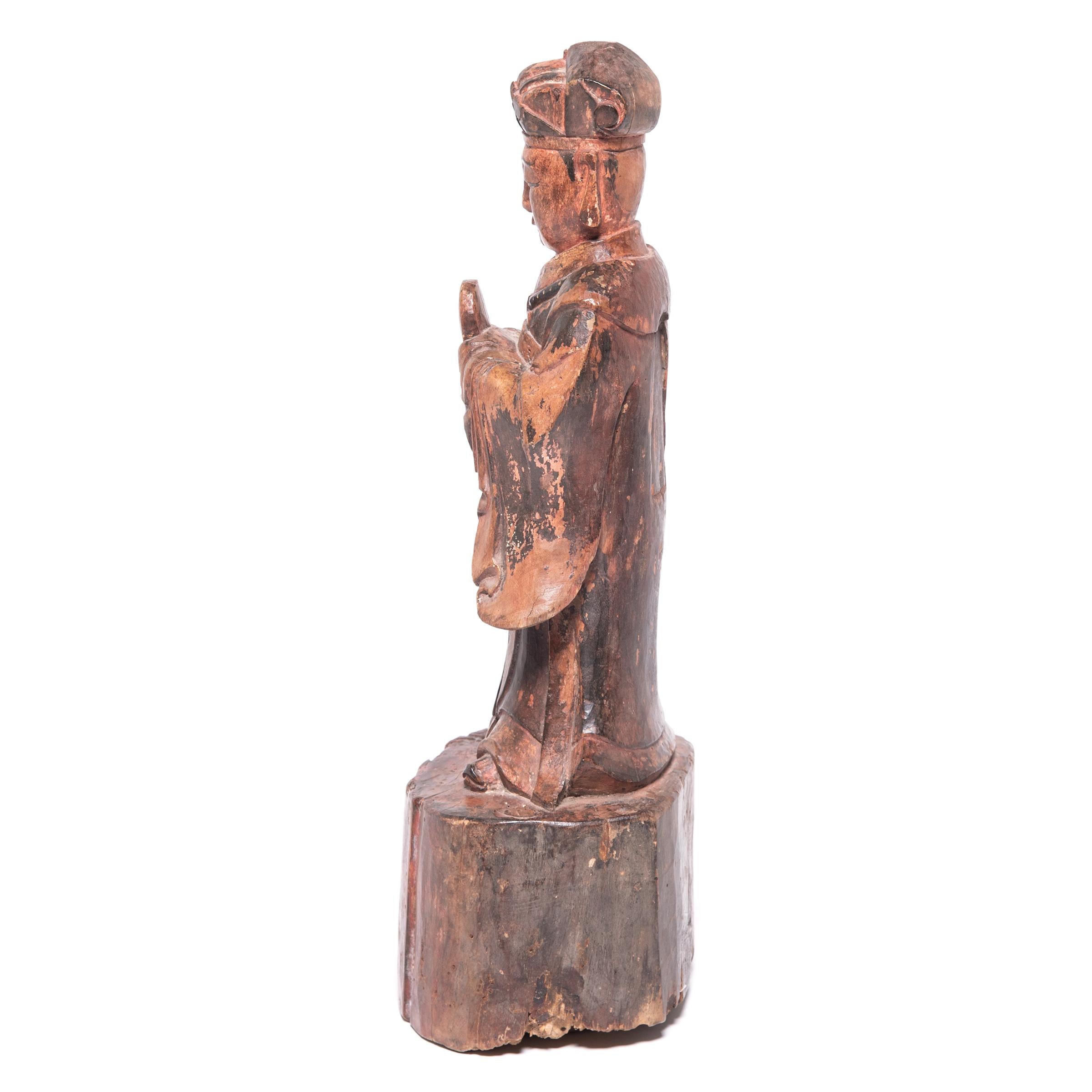 Carved in wood, this 19th-century figure of a spirit paid tribute to ancestors past on a traditional altar table. Allowing the base to reflect the wood’s natural state, the artist carved the figure with detailed robes and distinguishable features,