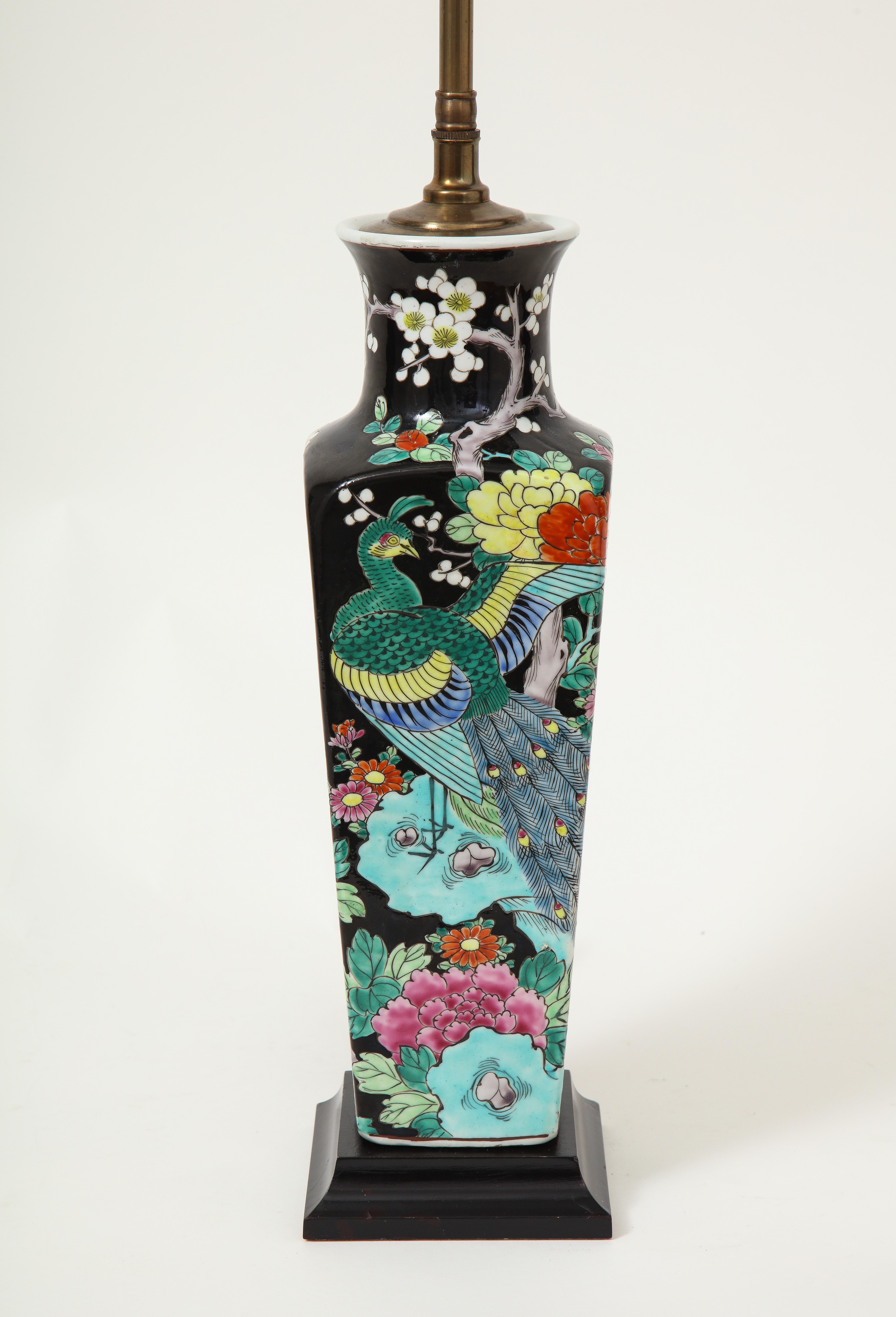 Of square tapering form; decorated with a peacock and tree peony branch in a bold polychrome palette; mounted on a black wood square base. Fitted with a brass adjustable rod and two moveable bulb sockets. Height to top of vase is 15.5 inches.
