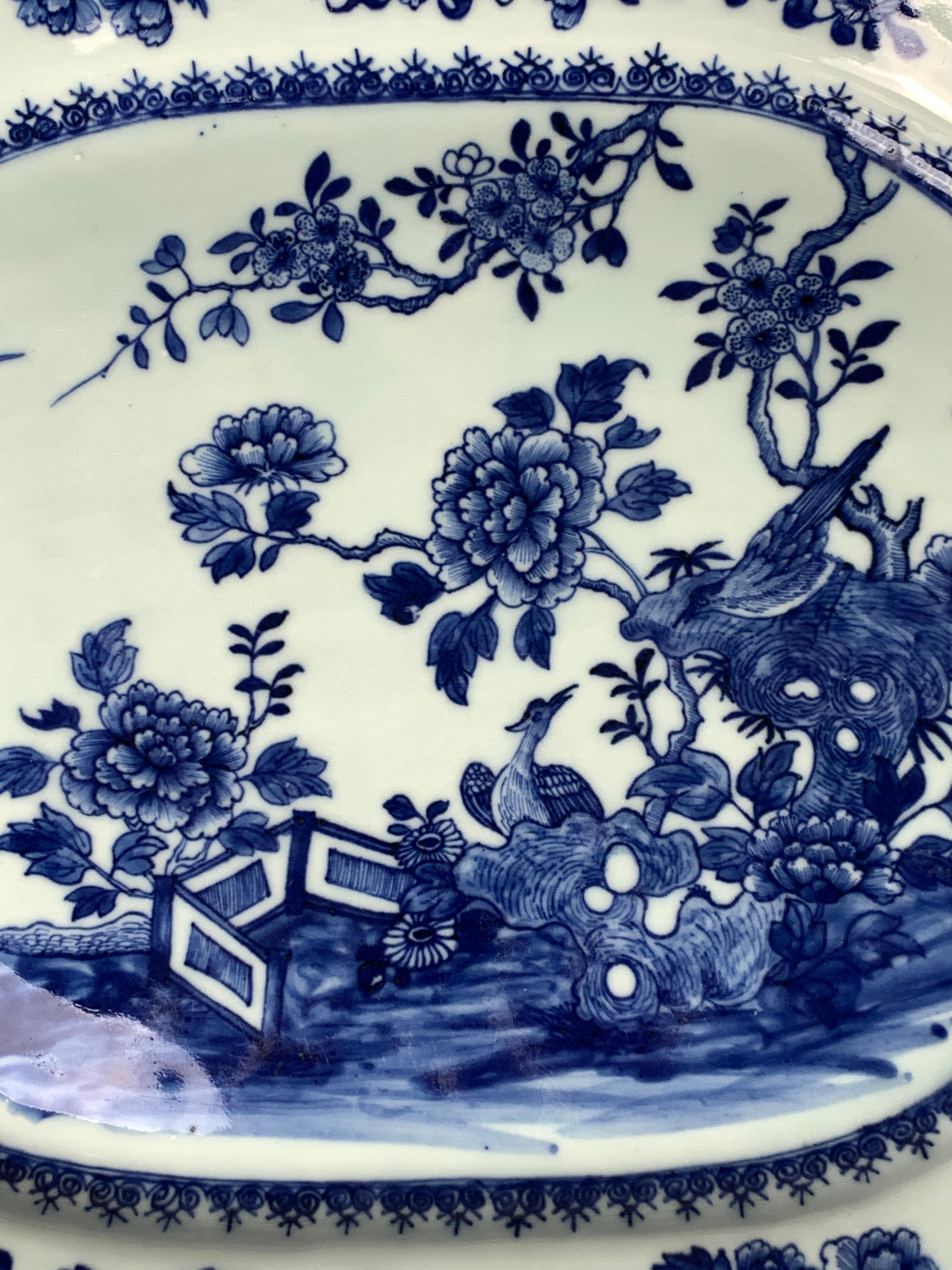 A Chinese blue and white porcelain platter hand-painted in the Qianlong dynasty in the 18th century. We see a beautiful garden scene painted in deep cobalt blue with large peonies emanating from rockwork, a pair of songbirds, and a second pair of