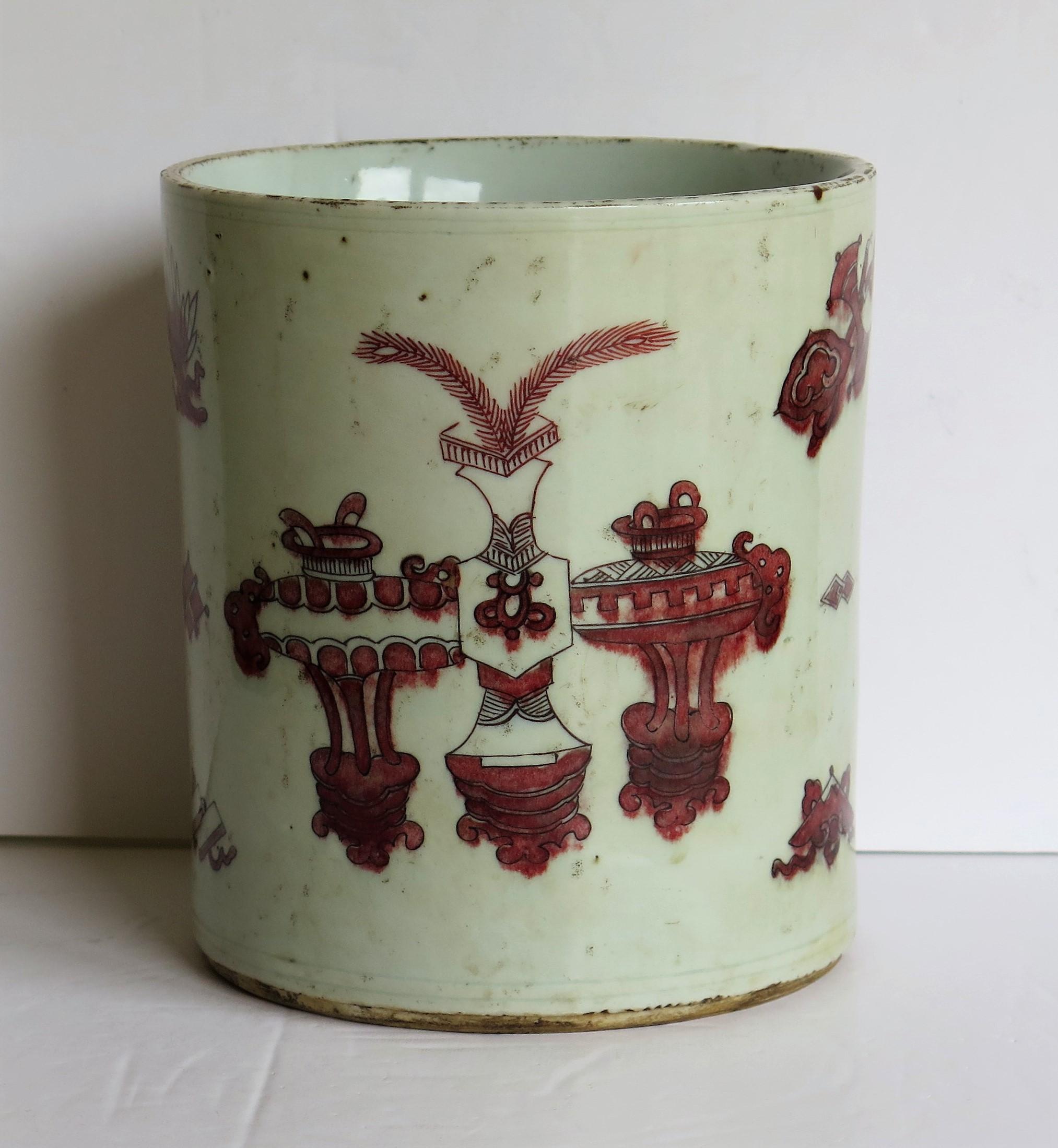 This is a very good Chinese porcelain Brush Pot or Bitong hand painted, under-glaze, in red / red-brown enamels with antiques, incense burners, precious things and other motifs and symbols, which we date to the 18th century, Qing period.

This piece