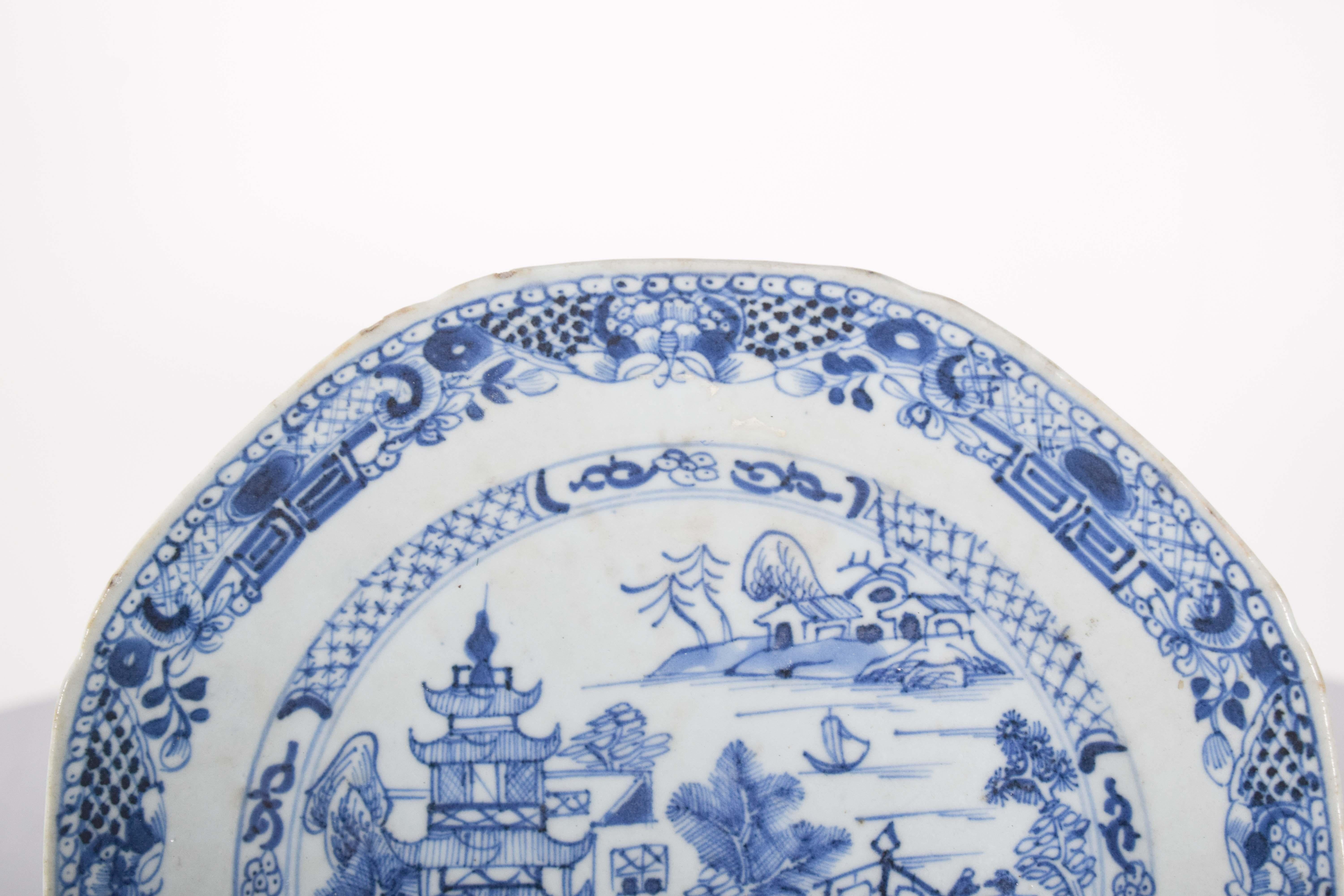 Tiefer Teller aus chinesischem Porzellan, für den Export. Blau-weißer Dekor mit Pflanzenmotiven, in der Mitte eine Flusslandschaft mit einem Boot, einer Brücke, einem Haus und einer Pagode. Qing-Dynastie, Qianlong-Periode (1736-1795).
Die zentrale