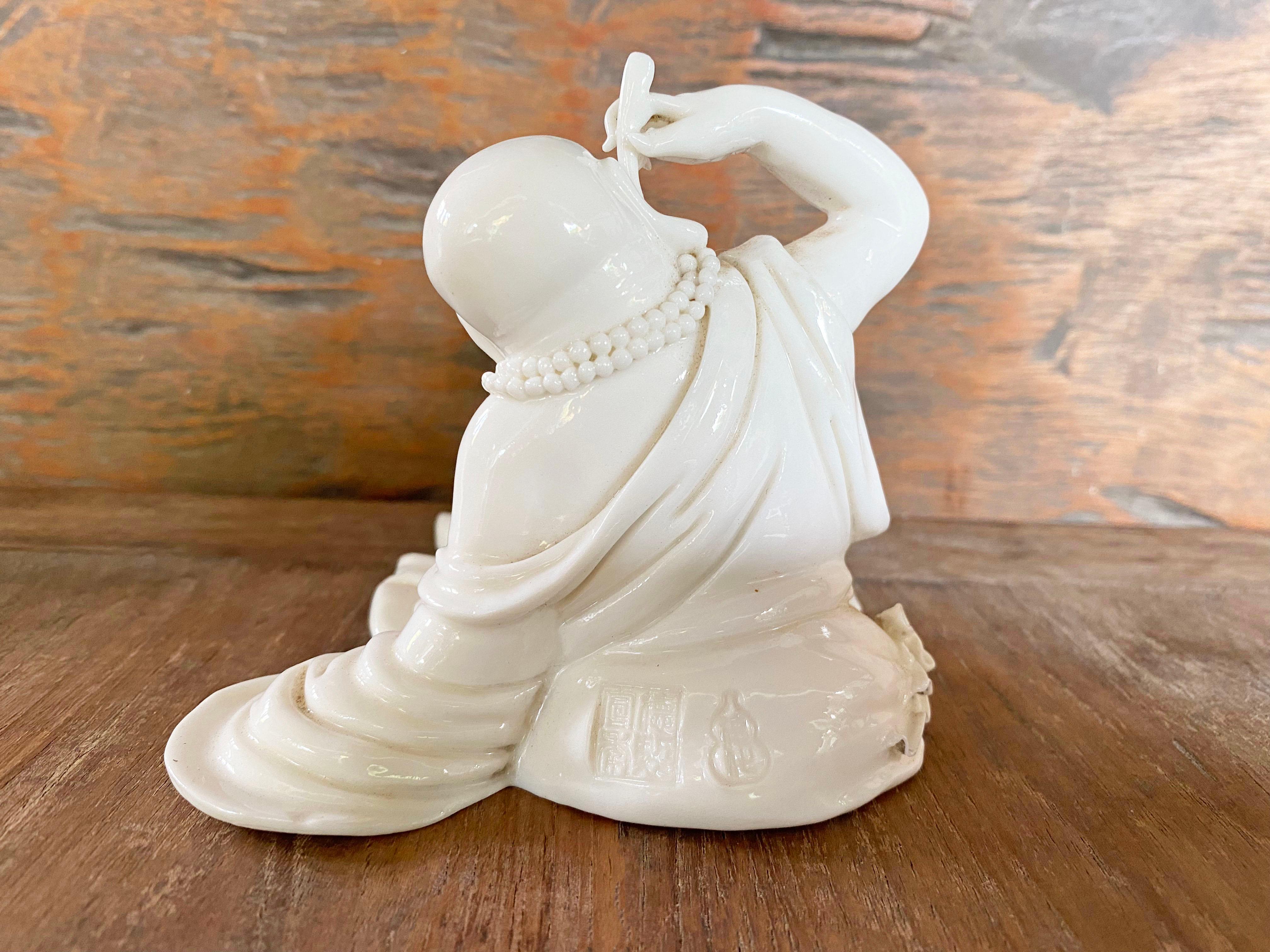 This Chinese Porcelain Dehua depicts a seated Budai (Chinese Monk) wearing a loose robe. It orginates from the Kilns o Dehua in China's Fujian Province. Dehua porcelain is regarded for it thick, lustrous and clear white glaze. Dehua is sometimes