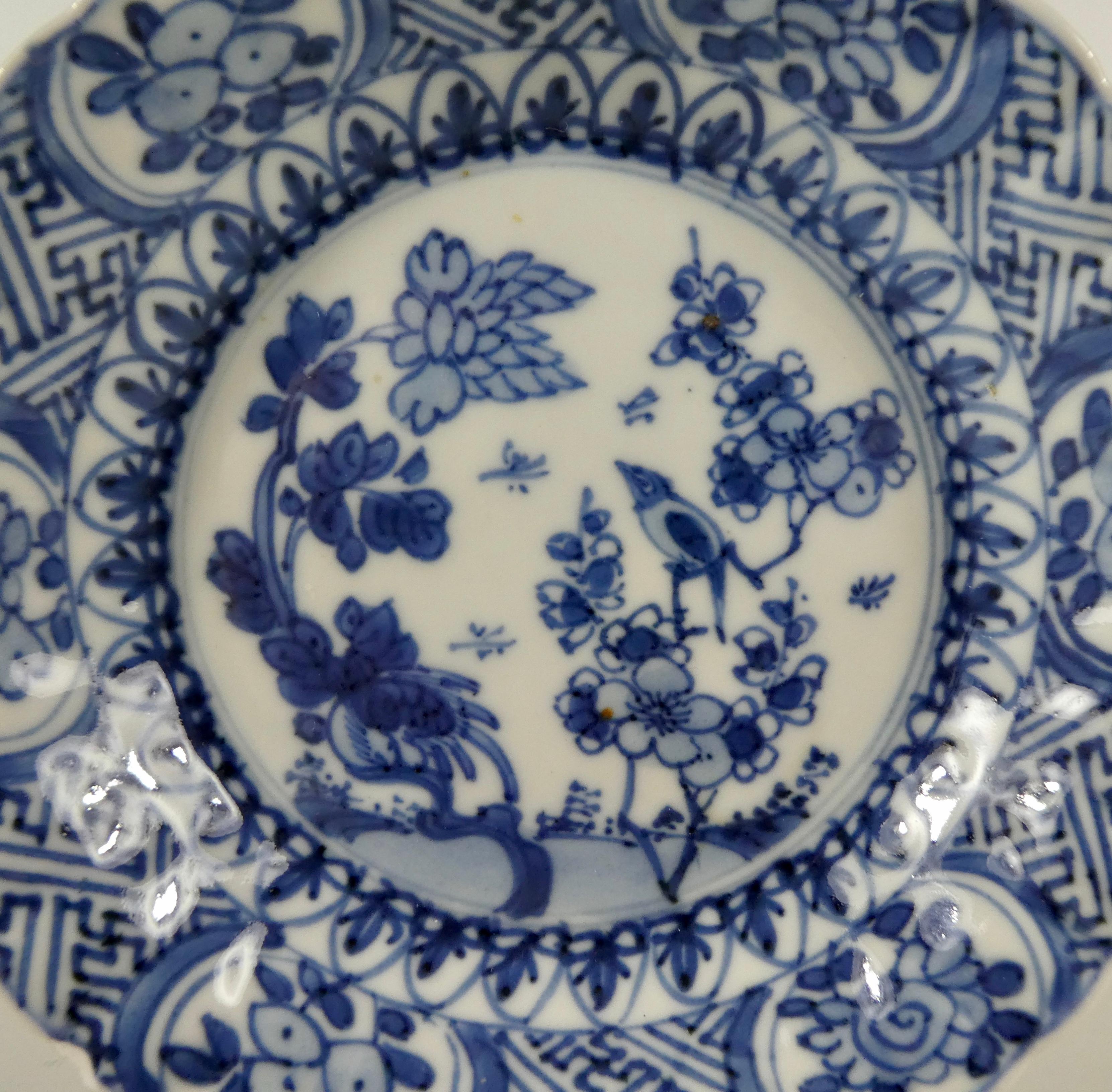 A small Chinese porcelain dish, Kangxi period, 1662-1722. The moulded dish, painted in underglaze blue with a central panel of a bird, perched amongst flowering plants, observing insects within a lappet border. Panels of flowering plants, upon a