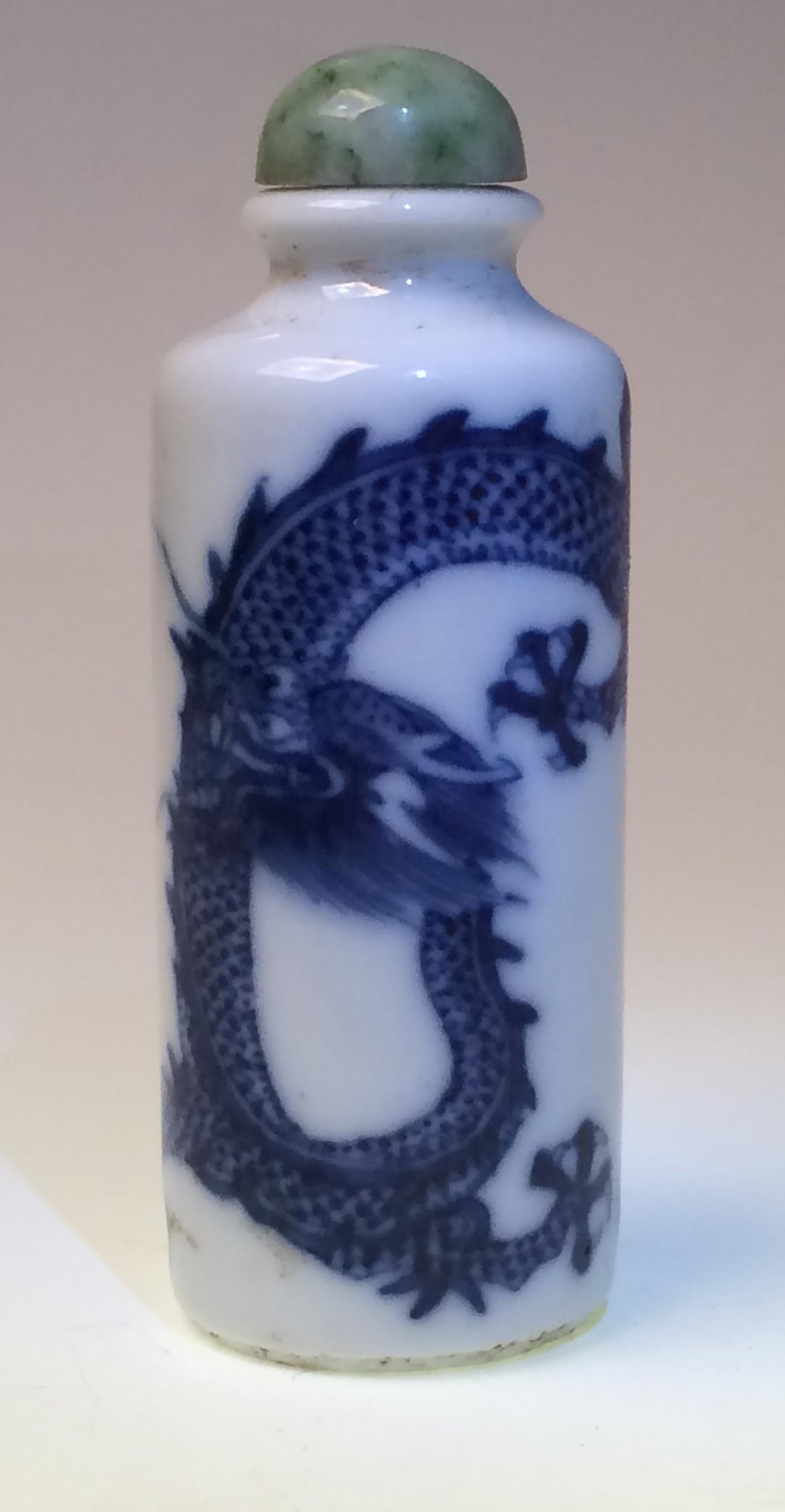 Chinese porcelain dragon snuff bottle, cylindrical pillar form with high shoulder, short neck, everted lip and concentric grooved base painted in underglaze cobalt blue of a single four clawed dragon wrapped around the body chasing a flaming pearl,