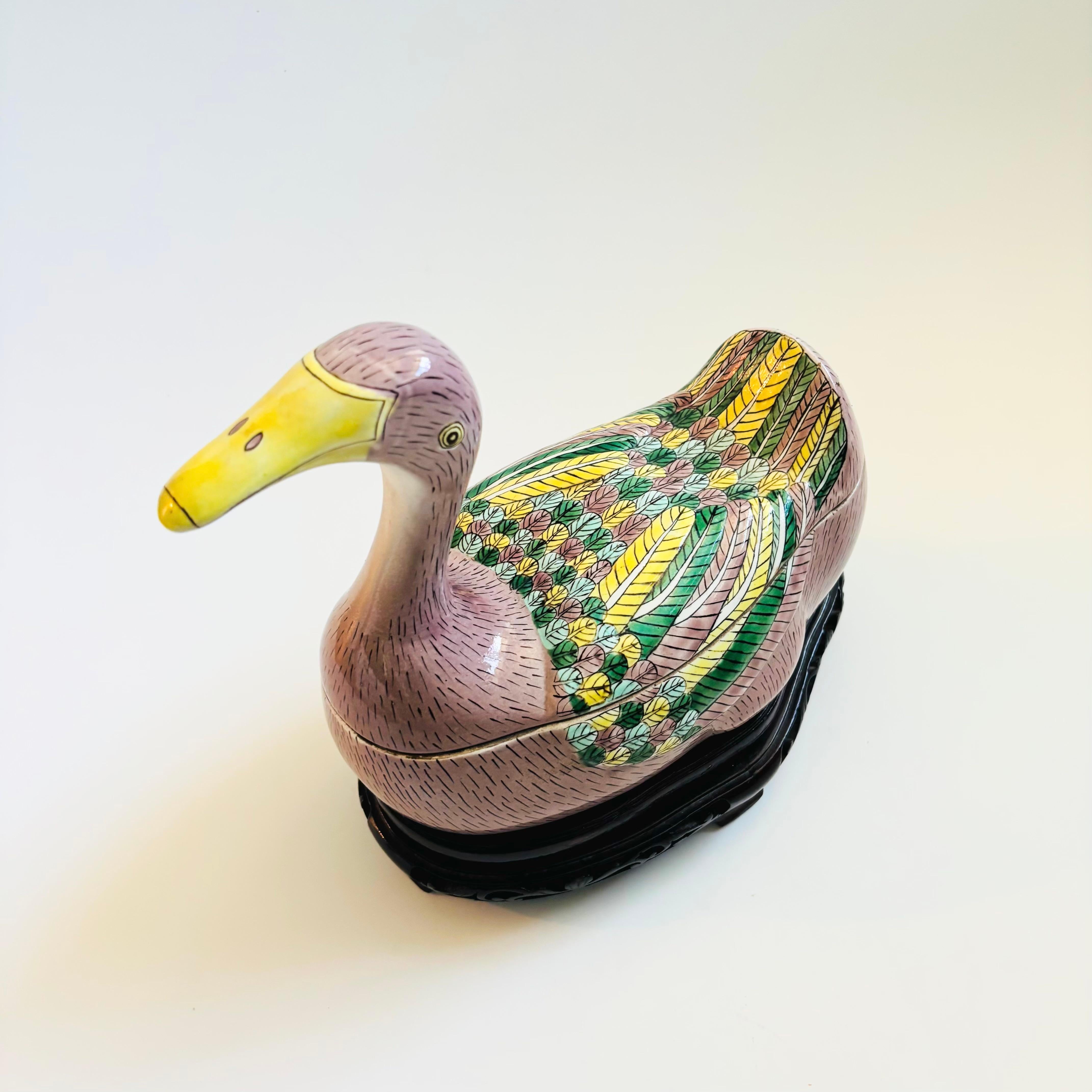 A large Chinese porcelain duck tureen. Beautifully detailed features and hand painted glazes. Uncommon pale purple glaze with vibrant yellows and greens at the feathers. Blue interior glaze. Comes with a fitted carved wood display stand. Estimated