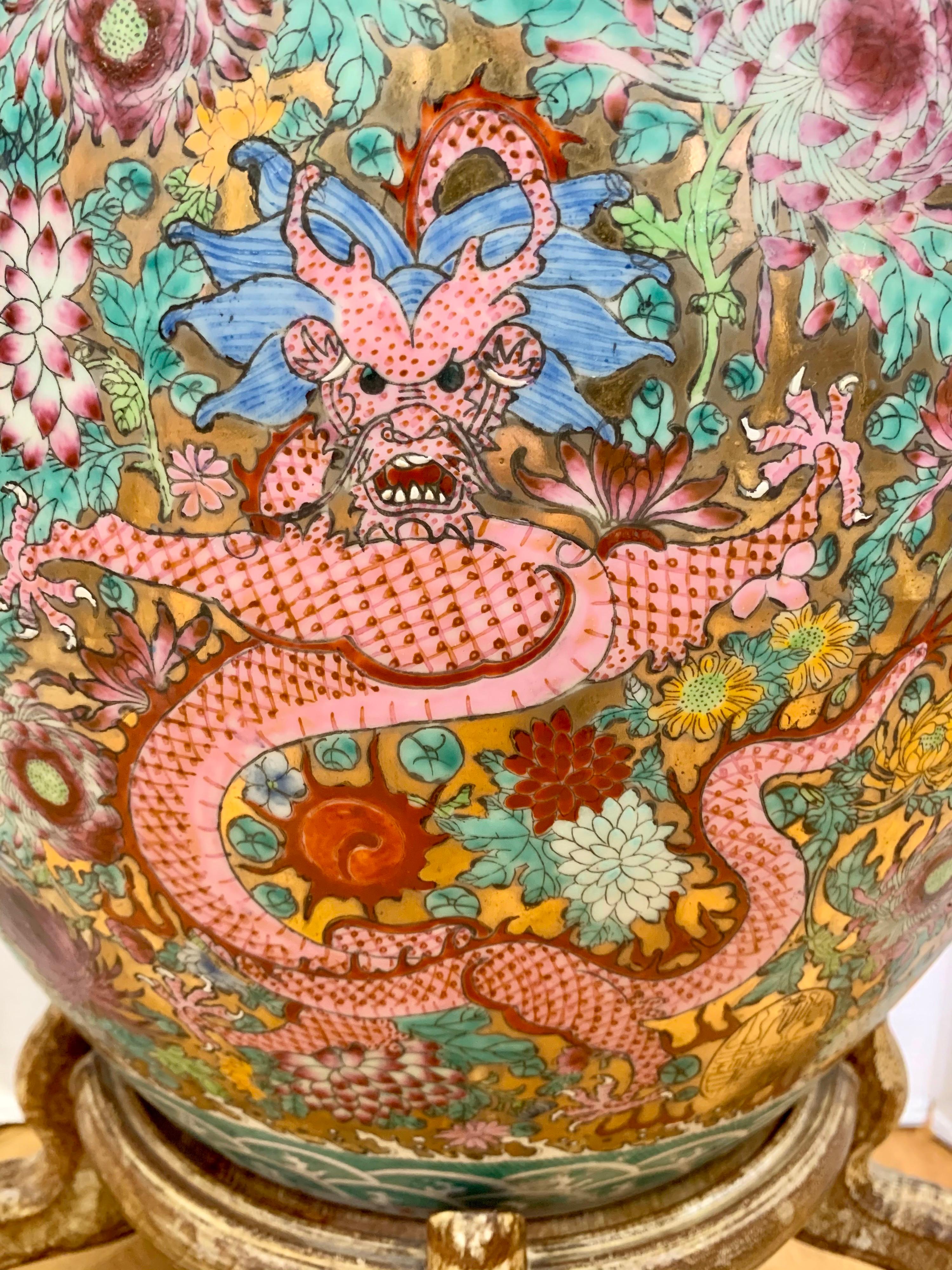 Exquisite Chinese porcelain jardinière planter features intricate hand painted colorful dragons on a gold metallic colored background with peonies and foliate decoration. Geometric decorates the top rim and base. It rests on a carved wood base.