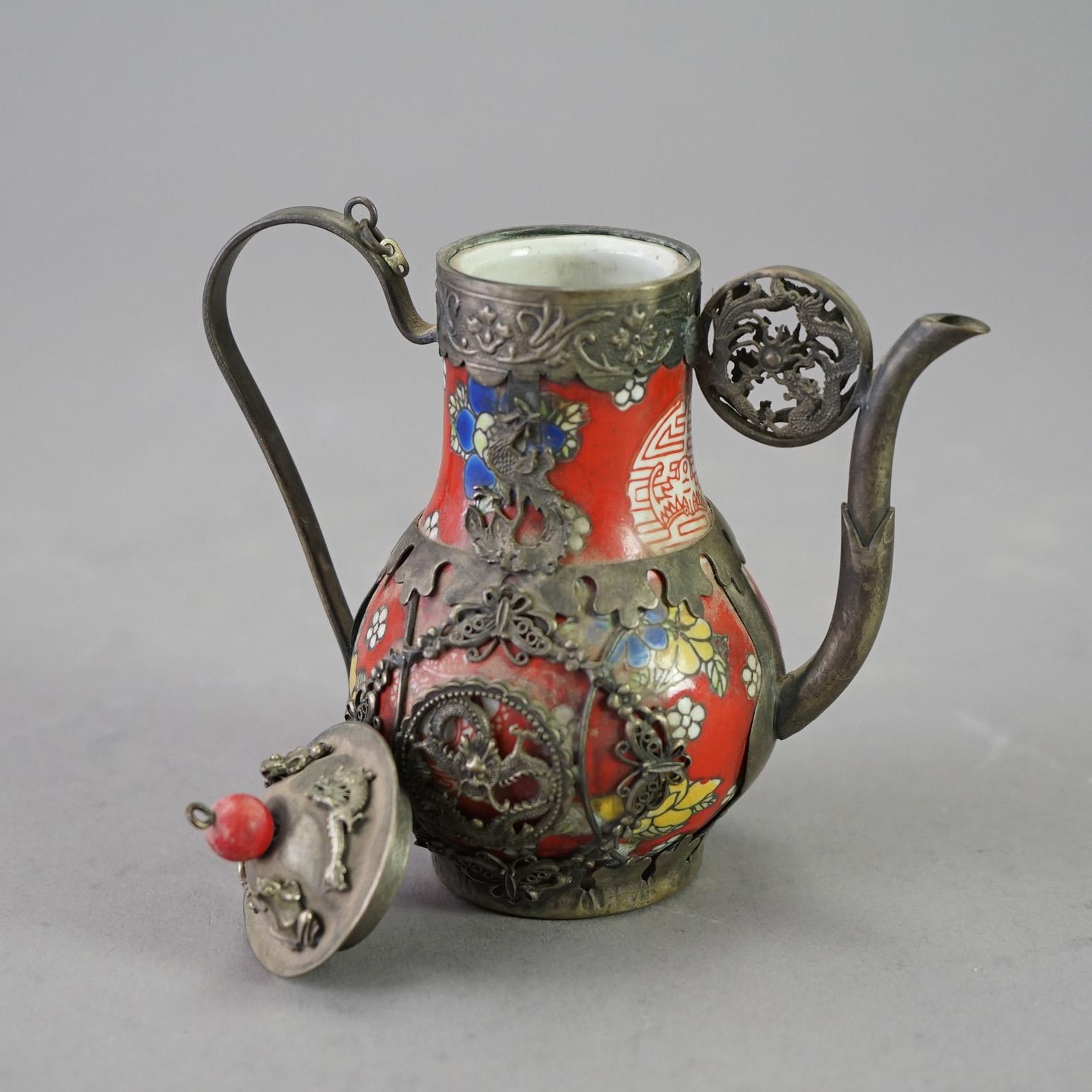 A miniature Chinese teapot offers porcelain vessel having floral design and silver overlay with dragons, frogs, and butterflies, stamped as photographed, 20th century

Measures- 5''H x 5''W x 3''D