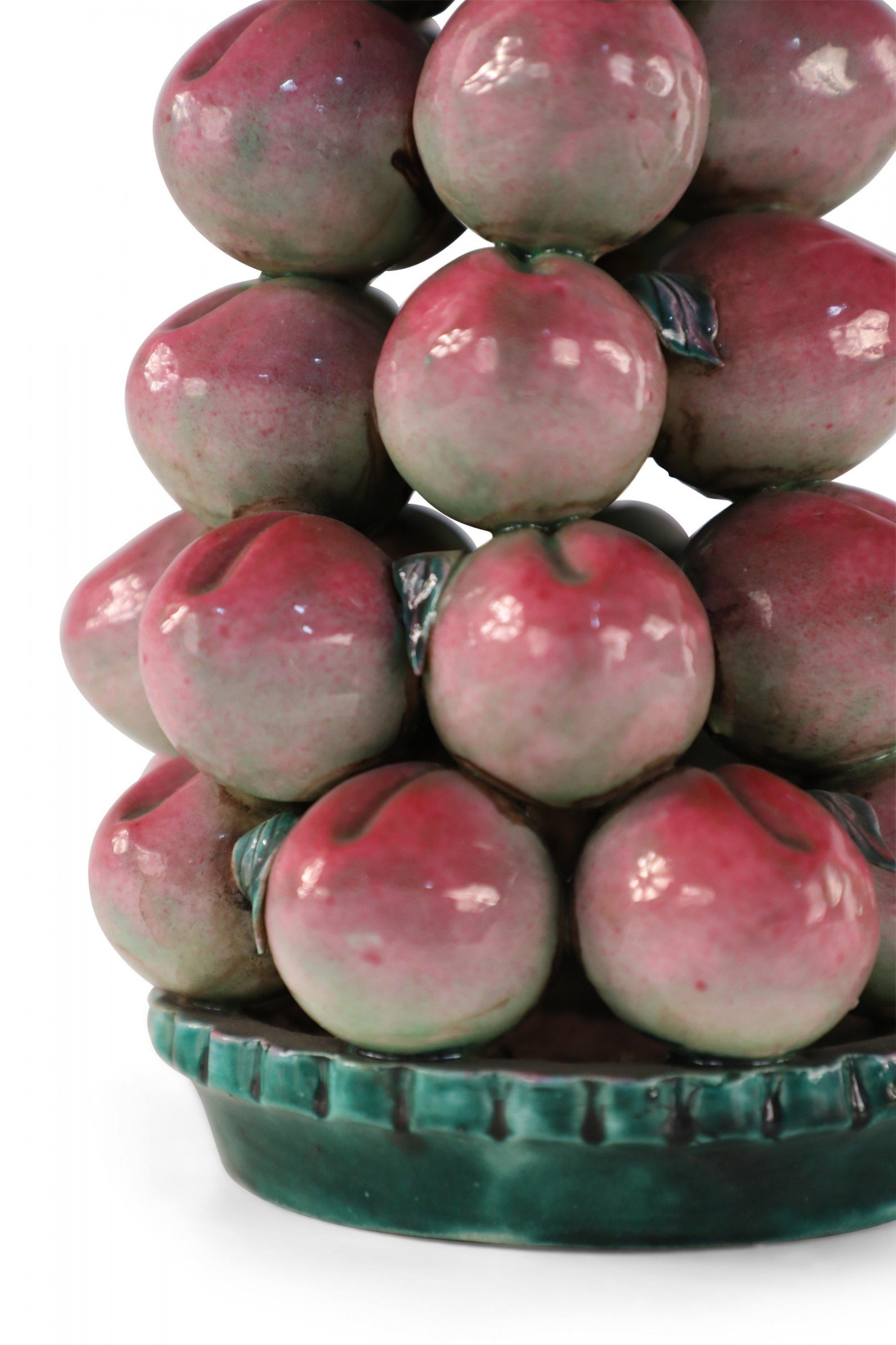 Chinese porcelain sculpture of ripe, red peaches - symbolizing immortality - each crafted with great detail, stacked high in a green dish as an abundant tribute to be placed at an altar.
 