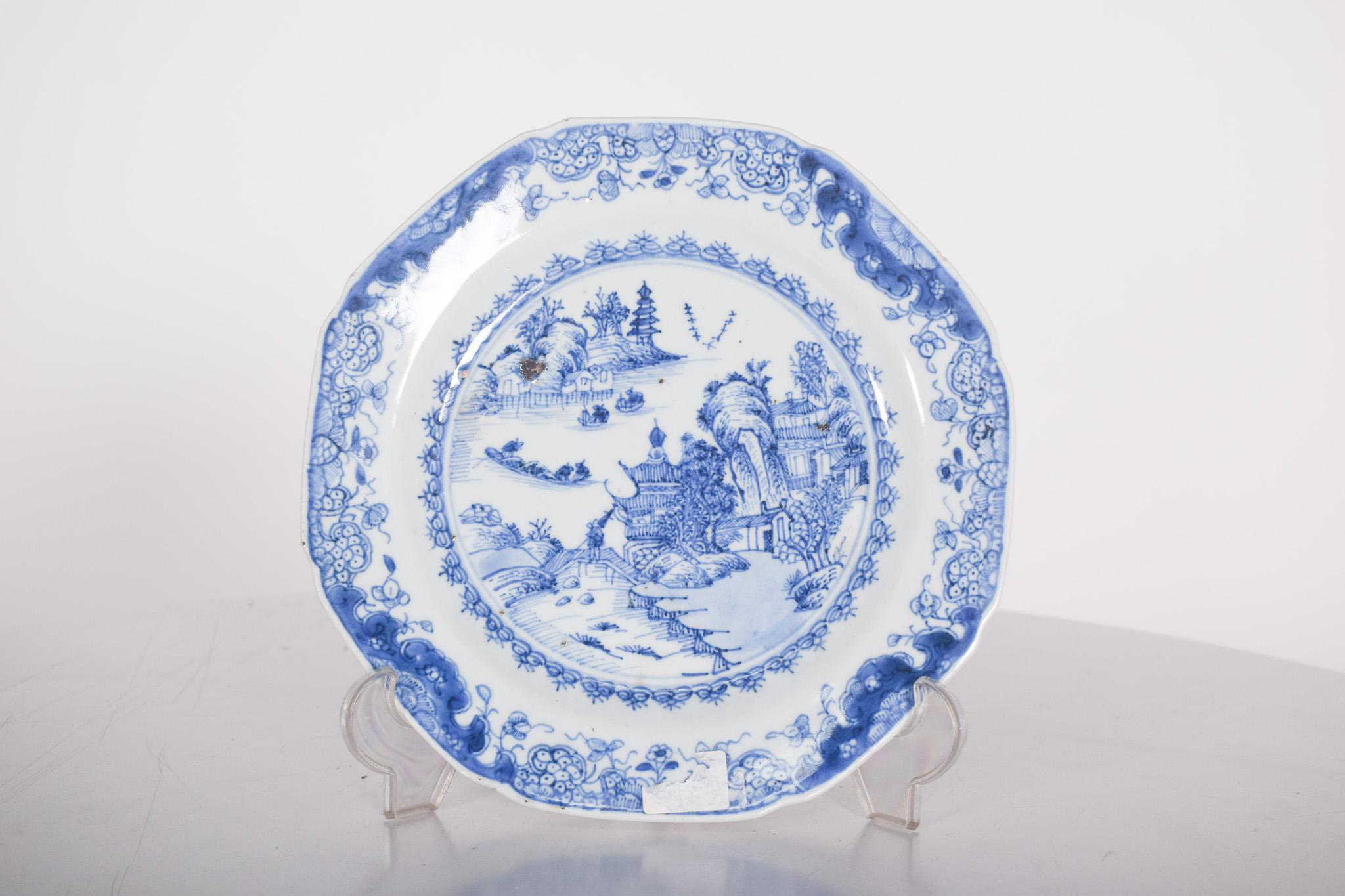 Chinesischer Porzellanteller für den Export. Blau-weißer Dekor, der eine Flusslandschaft mit Pflanzenmotiven, Booten, Brücke und Pagode darstellt. Qing-Dynastie, Qianlong-Periode (1736-1795).
In der Mitte des Tellers ist eine detaillierte bukolische