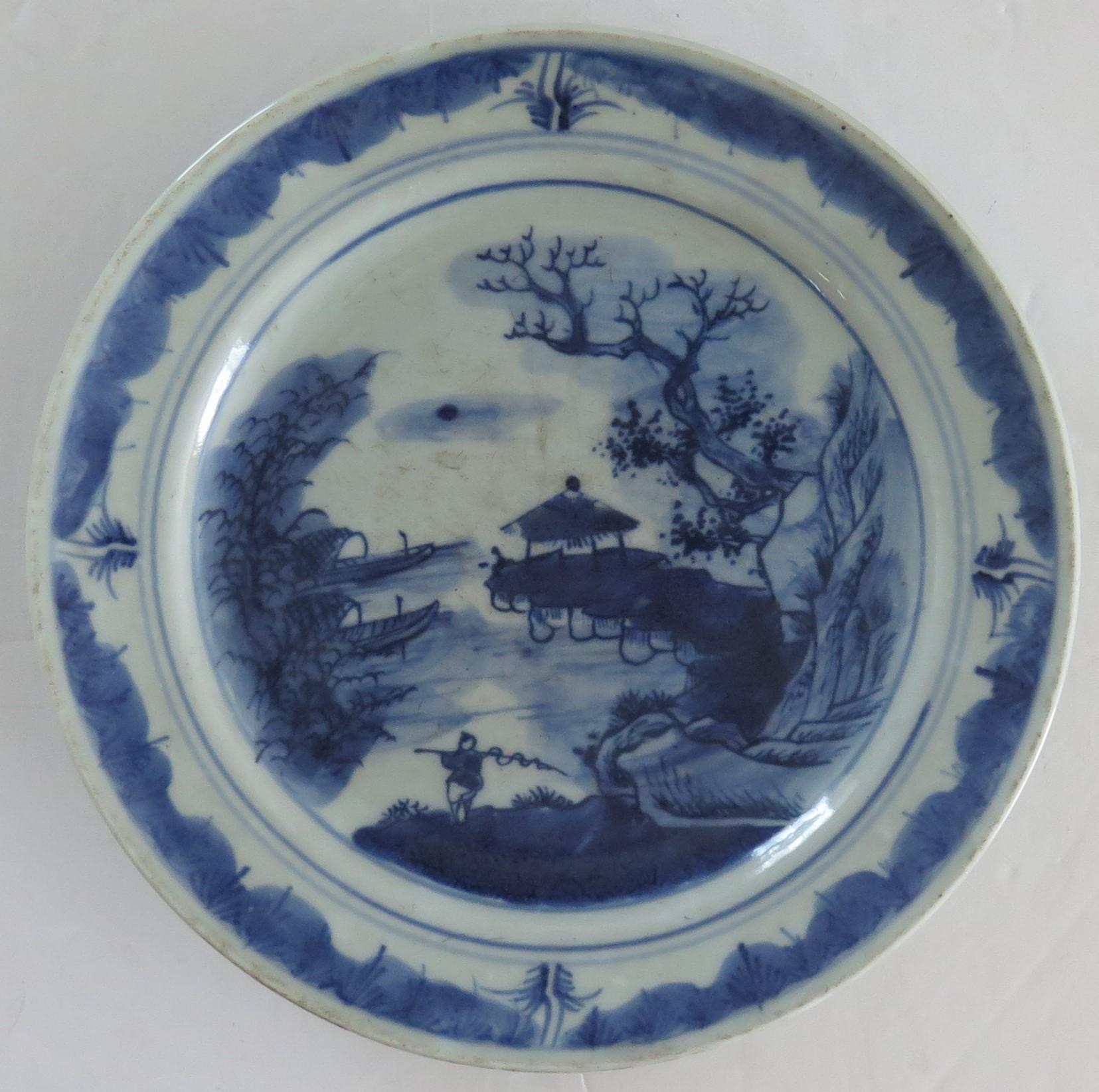 This is a good Chinese porcelain plate or dish with a blue and white, hand painted river scene, which we date to the Qing dynasty, late 18th century.

The dish or plate is fairly heavily potted and raised on a low foot. 

The plate has a light