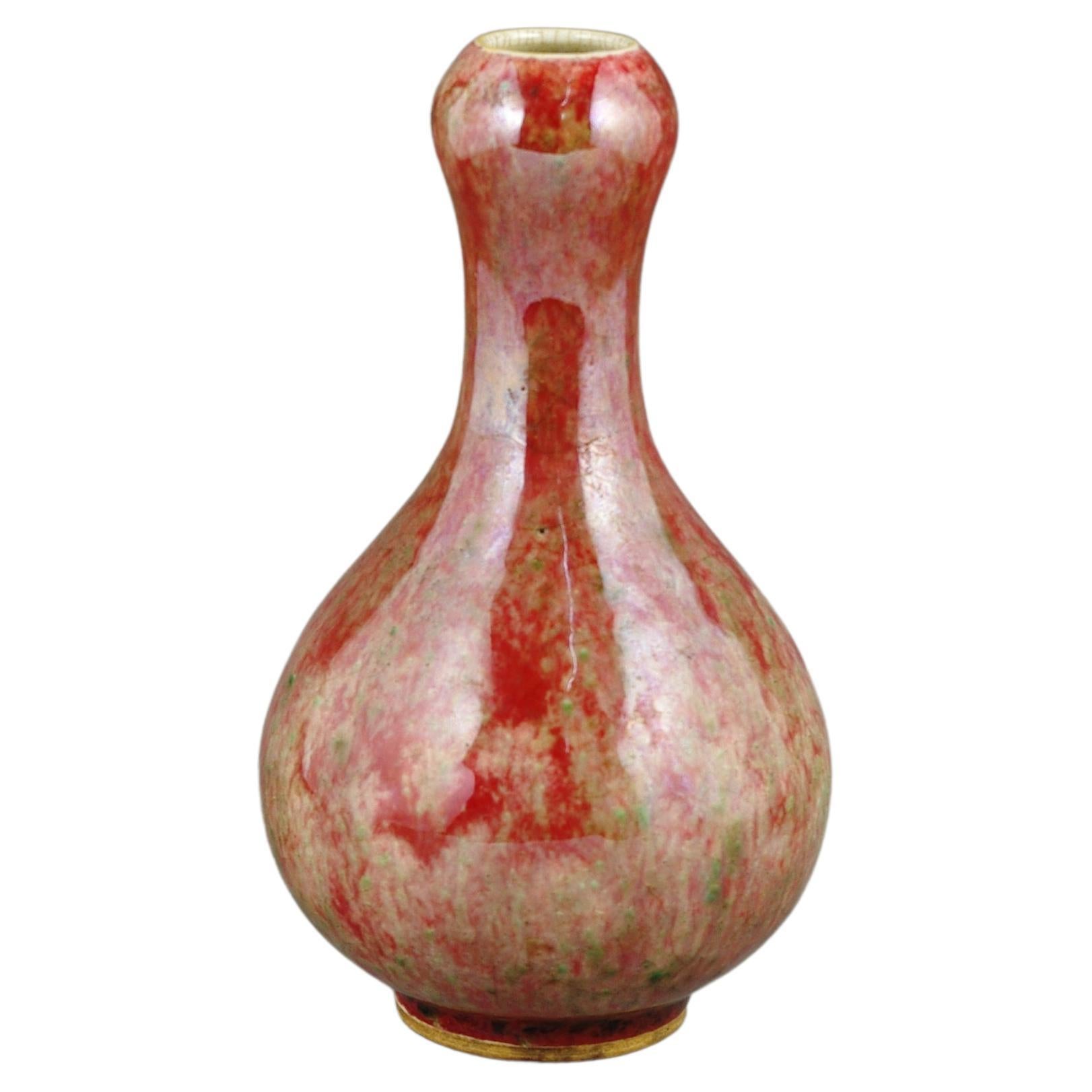 An antique early 20c peachbloom flambe garlic mouth vase. This vase is a magnificent representation of the flambe glazing technique, a process that gives it a fiery, flowing appearance, akin to the vibrant hues seen in a flame, making each piece a
