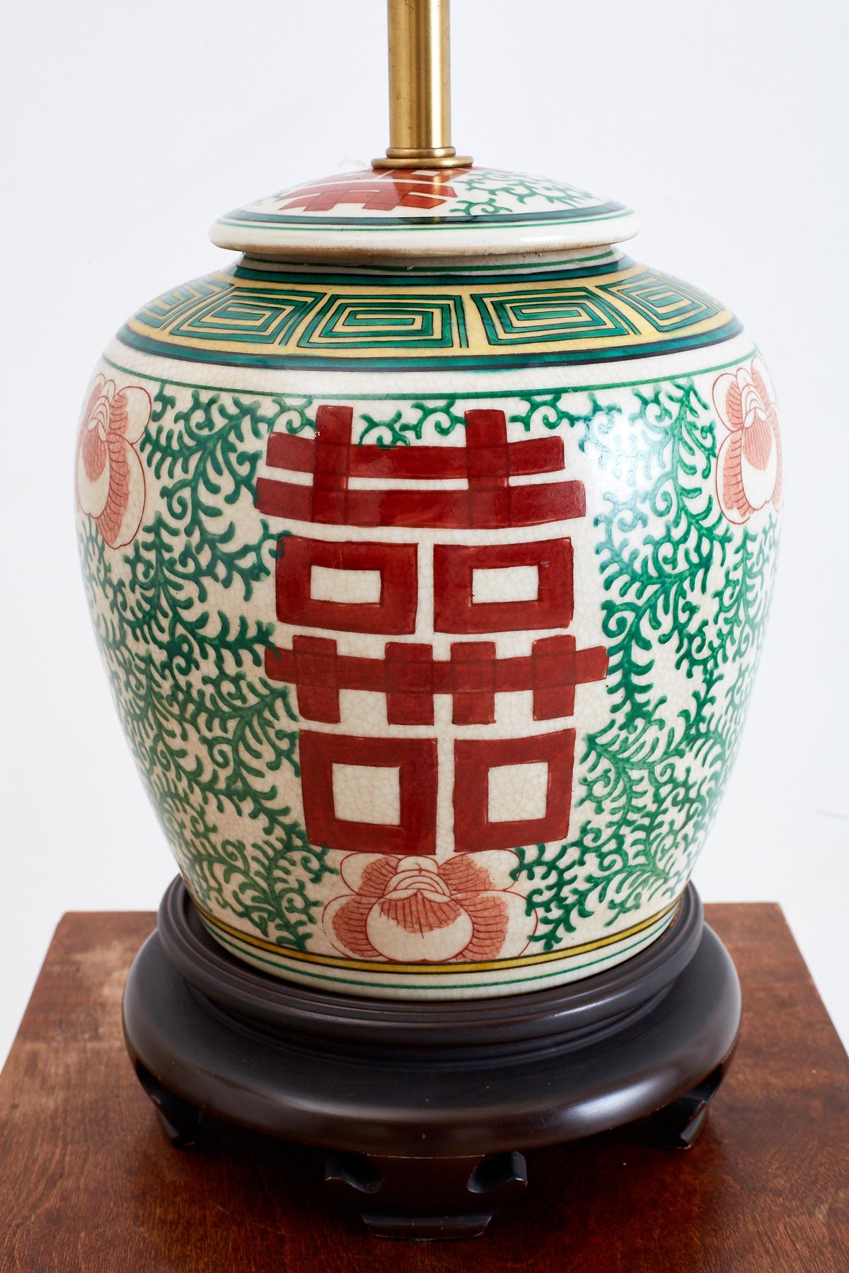 Cheerful Chinese porcelain ginger jar table lamp featuring a double happiness or wedded bliss symbol. The beautifully lidded jar is decorated with red Shuangxi symbols and green foliate designs over a light craquelure background. Topped with a dual
