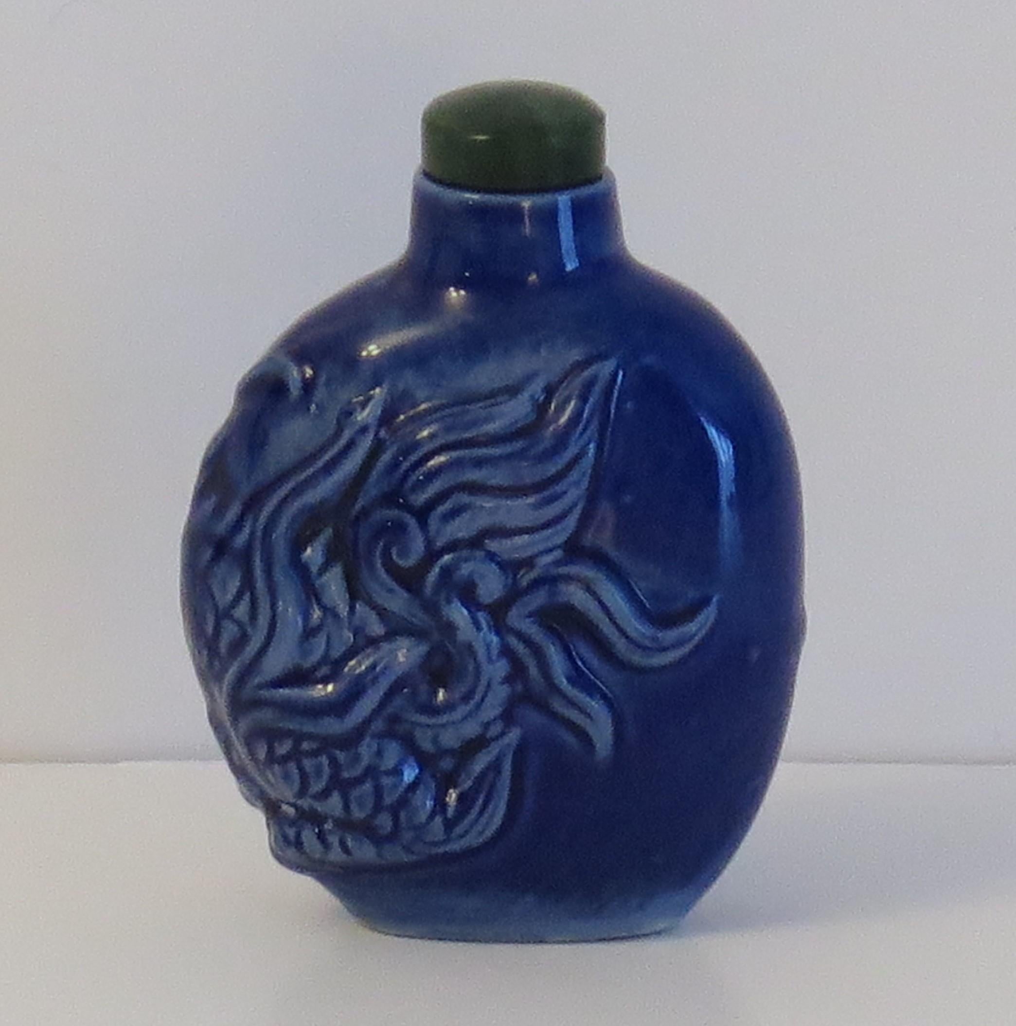 This is a good quality Chinese snuff bottle, made from porcelain with a moulded dragon and stone spoon top, circa 1930.

The ceramic bottle is potted with a molded mythical animal or dragon which covers both sides and one edge. It has been hand