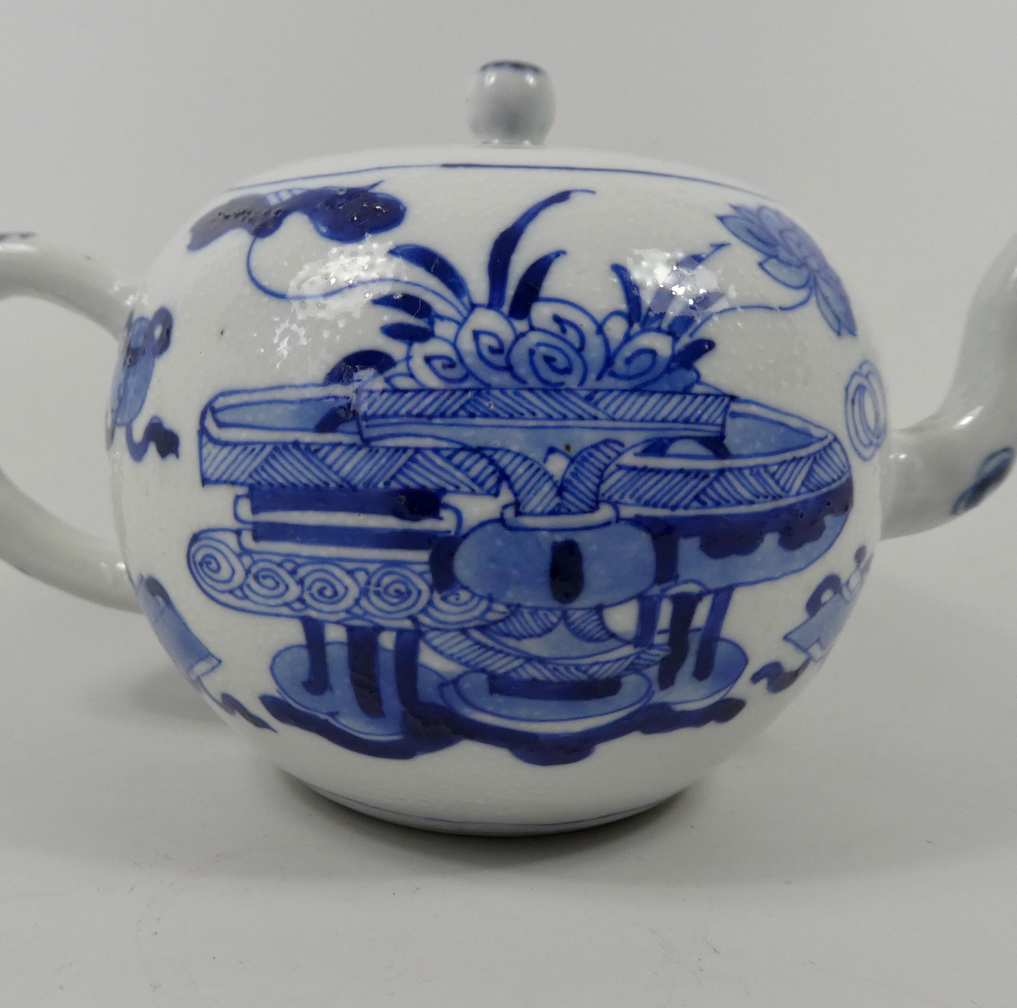 Chinese porcelain teapot, circa 1700, Kangxi Period. The lightly stippled ‘chicken skin’ body, well painted in underglaze blue, with panels of vases on stands, and Buddhistic symbols. The simple loop handle, and spout decorated with flowering