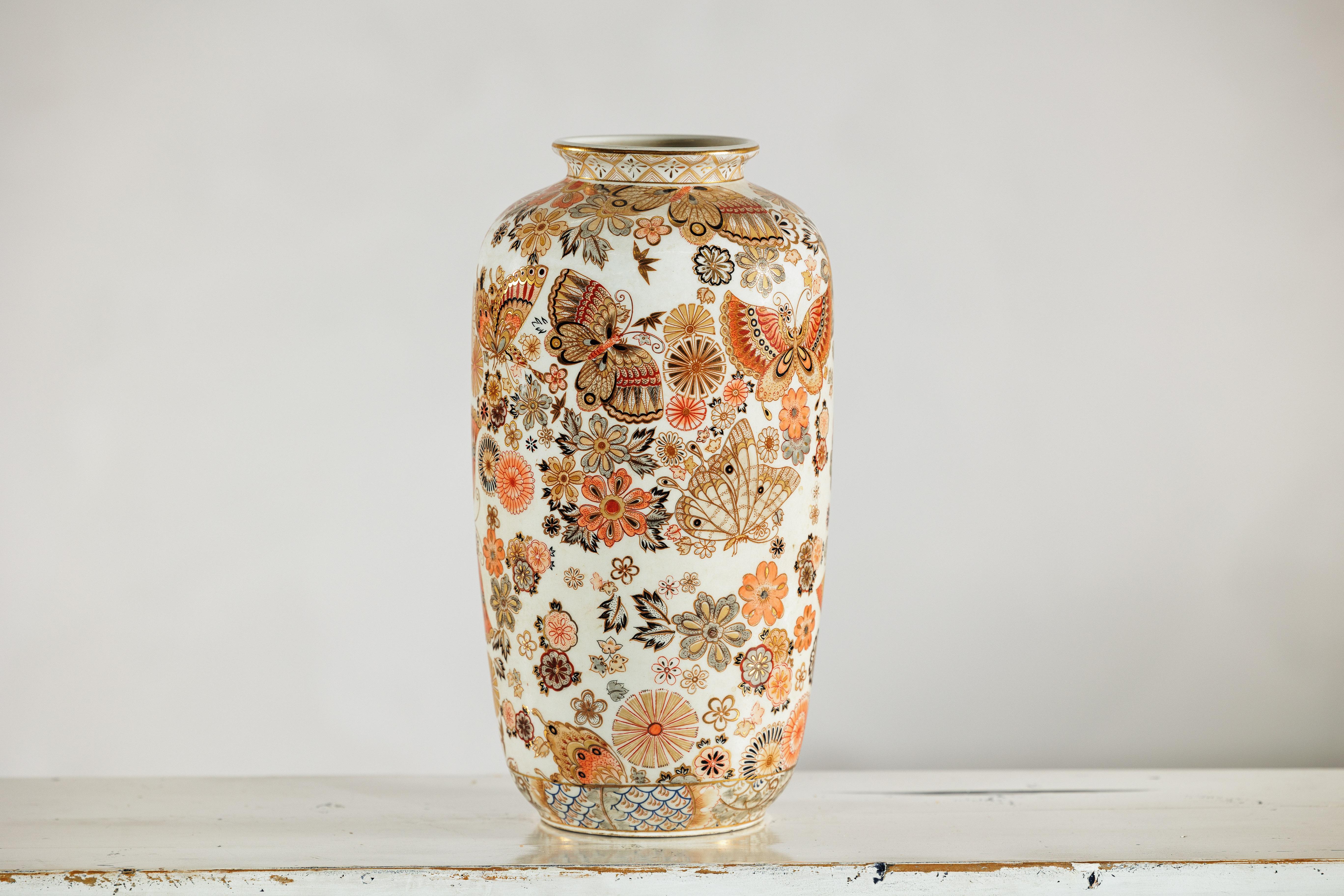 A Chinese porcelain vase decorated in the Japanese Kutani style, richly adorned with butterflies and floral motifs. The tall, slender form rises to a slightly flared rim, its white ground nearly covered in polychrome overglaze enamels in tones of