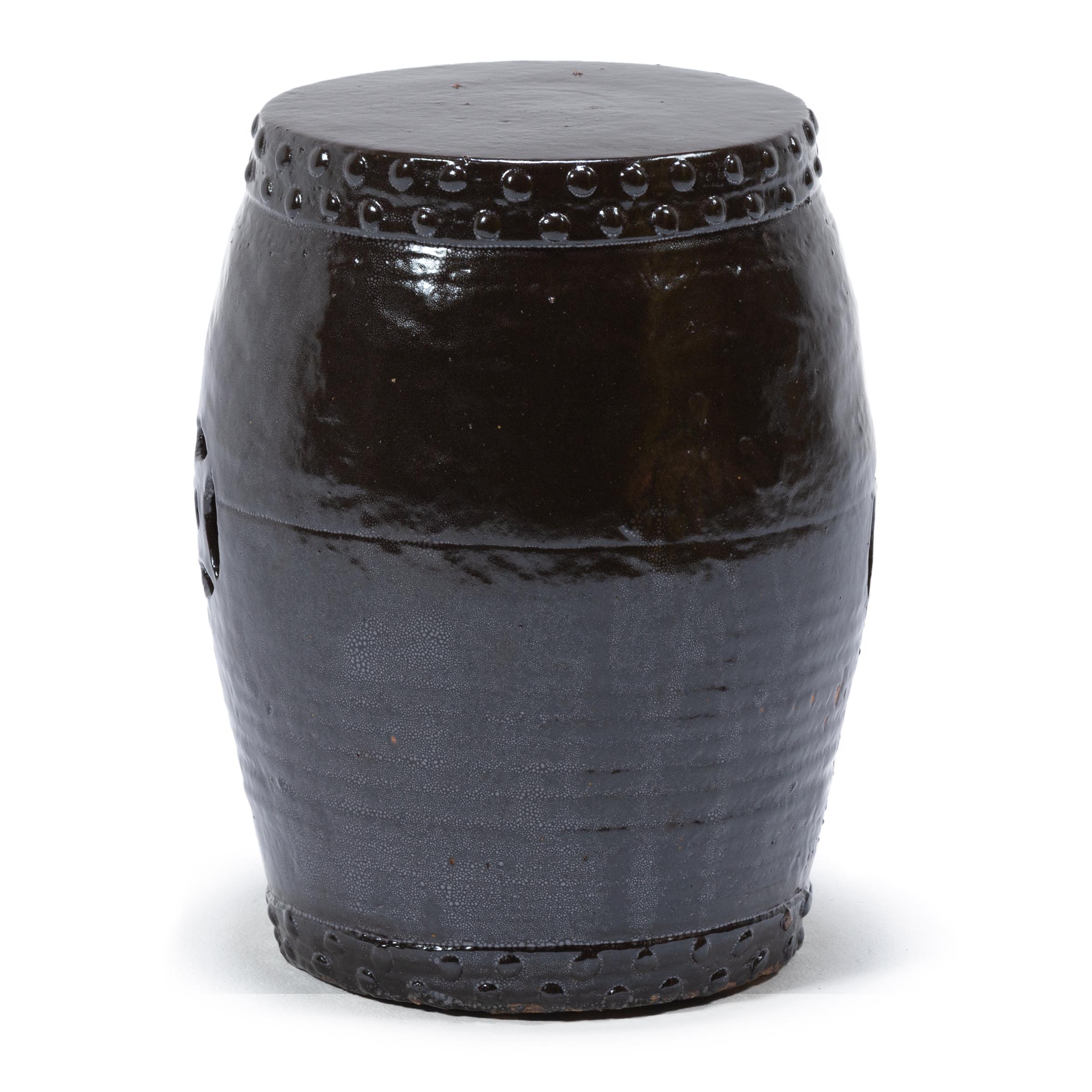 This early 20th-century ceramic garden stool from China's Zhejiang province keeps with tradition with its simple drum-form shape, cloaked in a dark brown-black glaze. Ringing both the top and bottom is a pattern of boss-head nails that imitate those