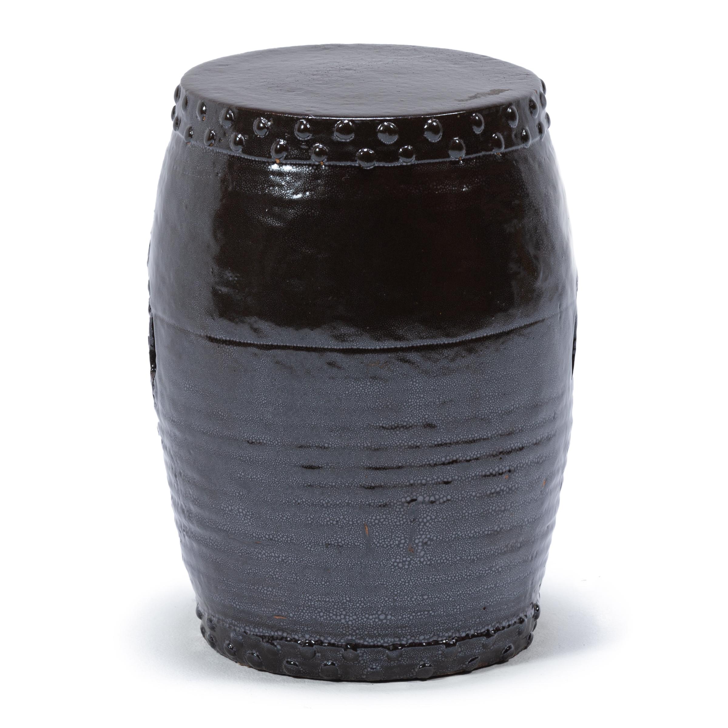 This early 20th century garden stool from China's Zhejiang province keeps with tradition with its simple drum-form shape, cloaked in a dark brown glaze. Ringing both the top and bottom, a pattern of boss-head nails imitates those used to stretch a