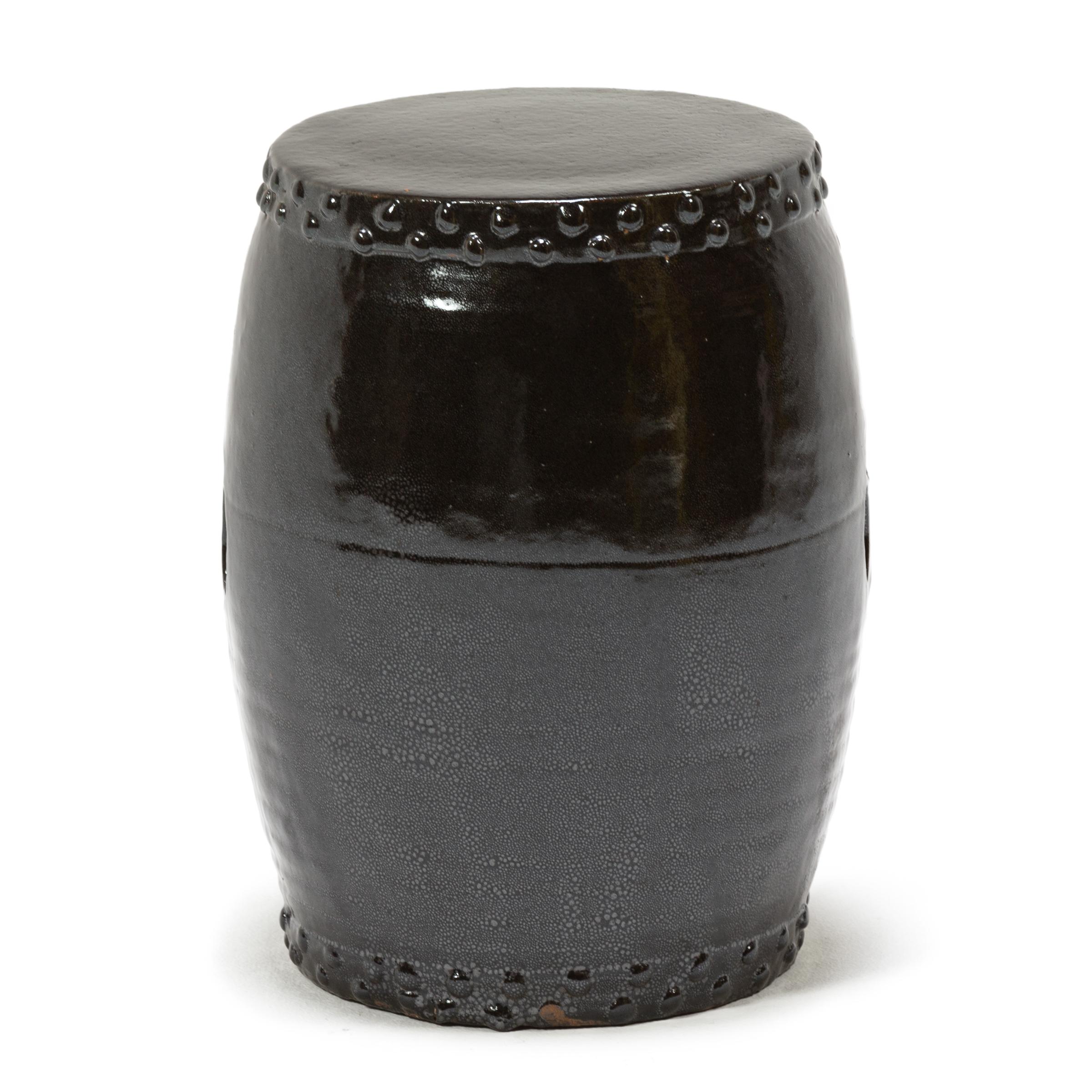 This early 20th-century garden stool from China's Zhejiang province keeps with tradition with its simple drum-form shape, cloaked in a dark brown glaze. Ringing both the top and bottom, a pattern of boss-head nails imitates those used to stretch a