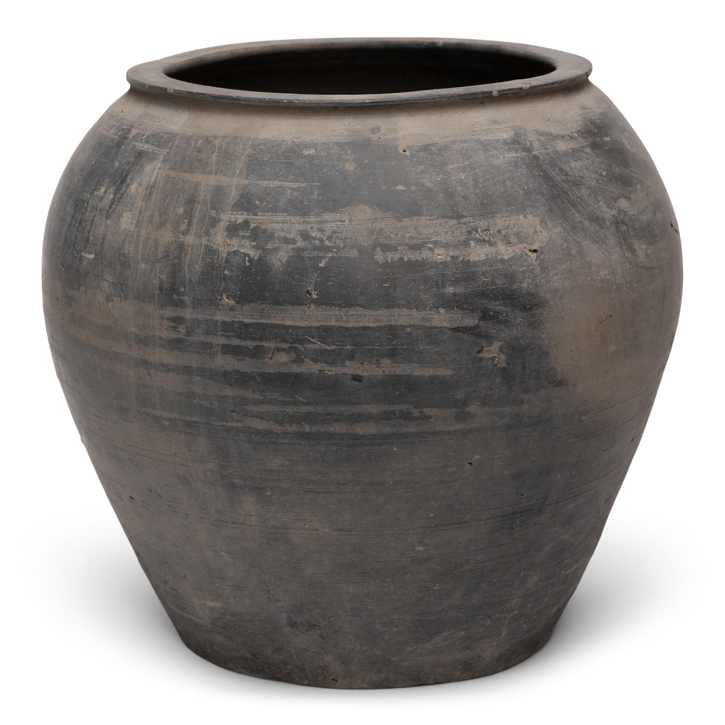 Scolpito all'inizio del XX secolo nella provincia cinese dello Shanxi, questo vaso in terracotta ha un esterno marrone-taupe fumoso con proporzioni equilibrate e una superficie non smaltata splendidamente irregolare. Con l'umile compito di