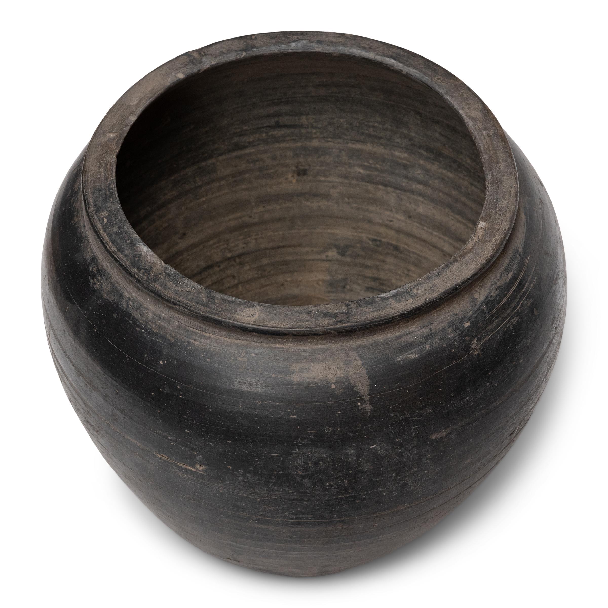 Sculpted during the early 20th century in China's Shanxi province, this terra cotta vessel has a smoky taupe-black exterior with balanced proportions and a beautifully irregular unglazed surface. Charged with the humble task of storing dry goods,
