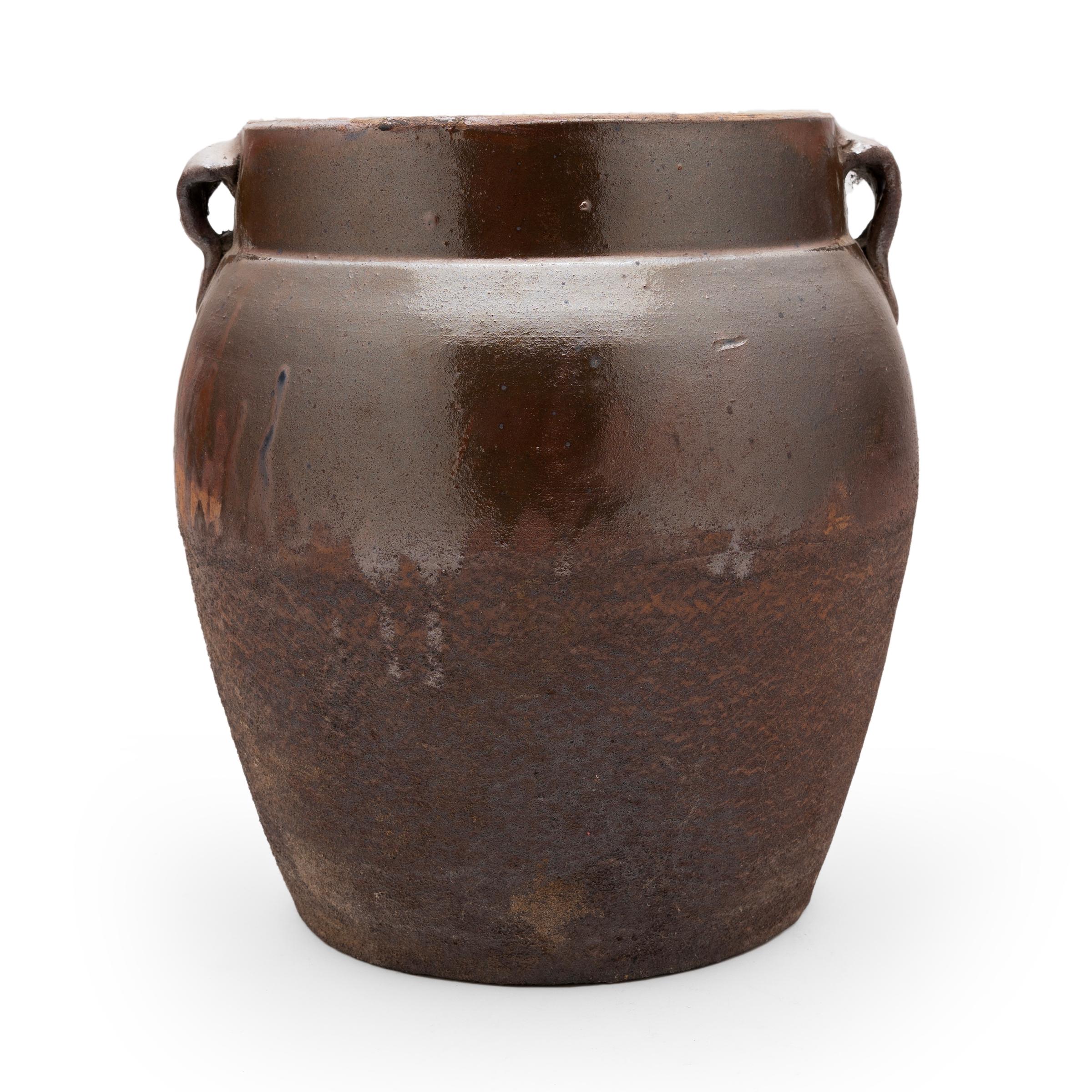 As evidenced by the interior glaze, this wide-mouth jar was once used in a provincial Qing-dynasty kitchen for storing food and condiments. The large vessel has a gently tapered form, with rounded shoulders, small strap handles and a short, straight